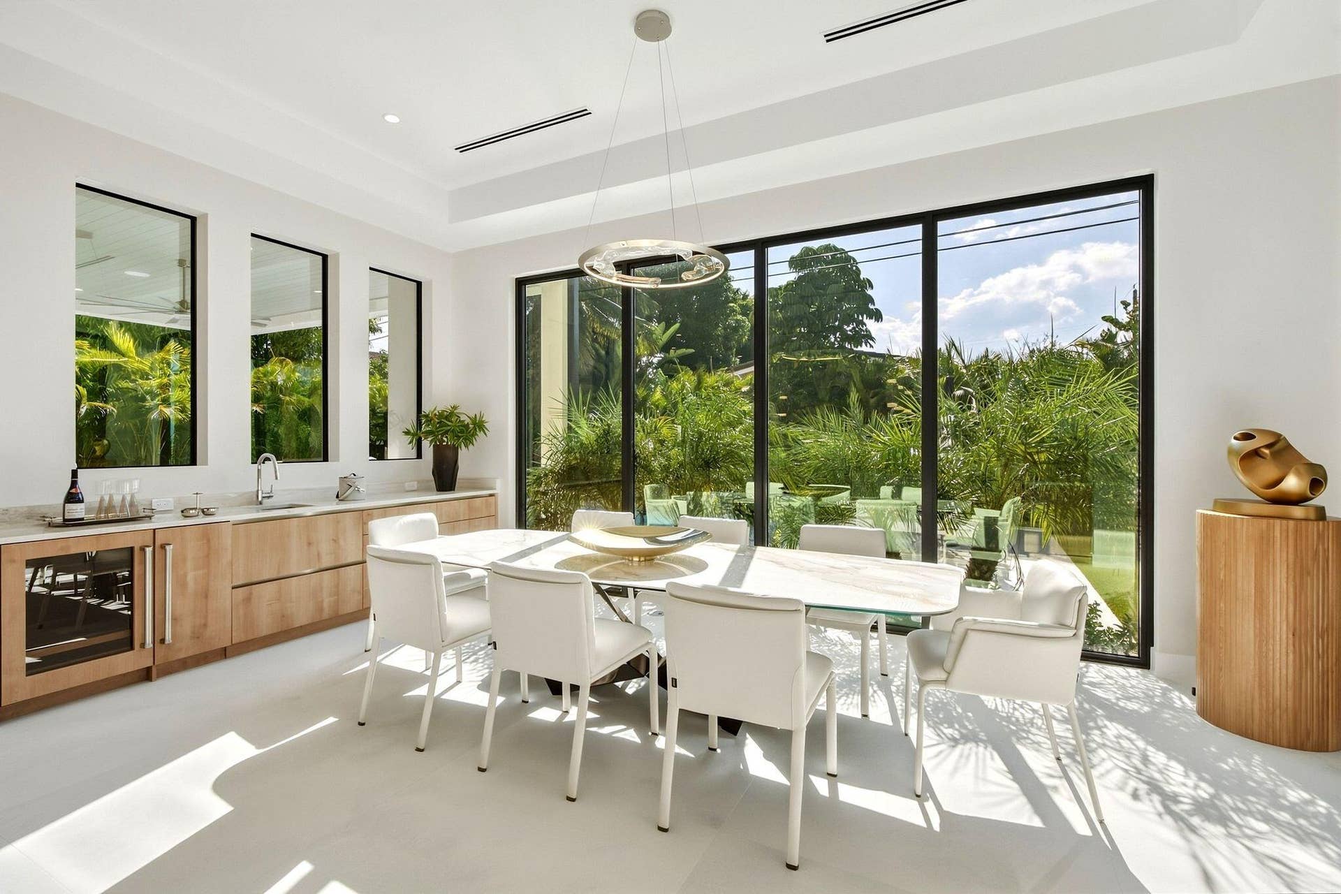 Expansive floor-to-ceiling windows, built-in bar with under-counter beverage cooler, recessed lighting, and a modern chandelier