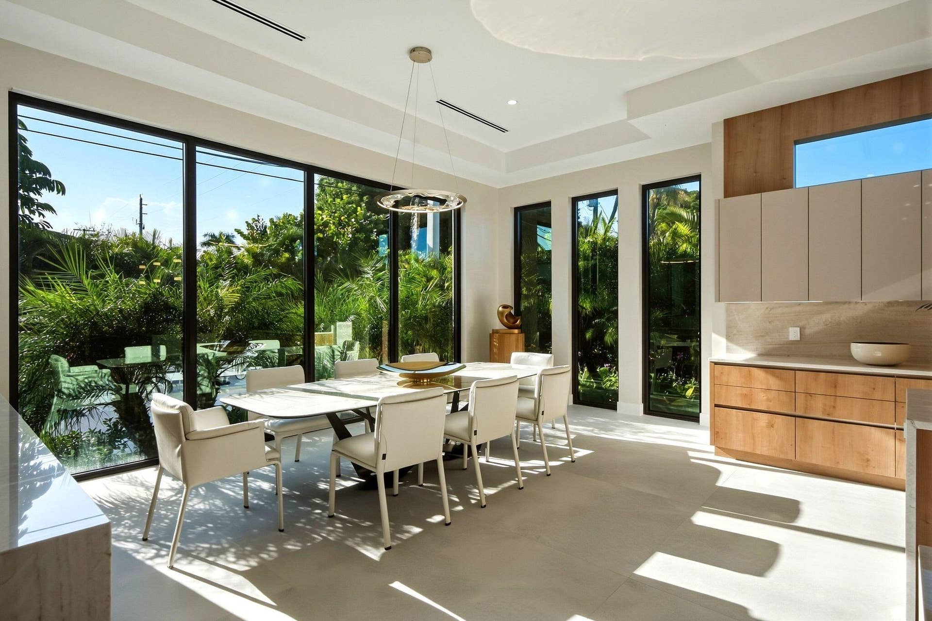 Floor-to-ceiling windows, recessed lighting, and a modern chandelier illuminate this dining space