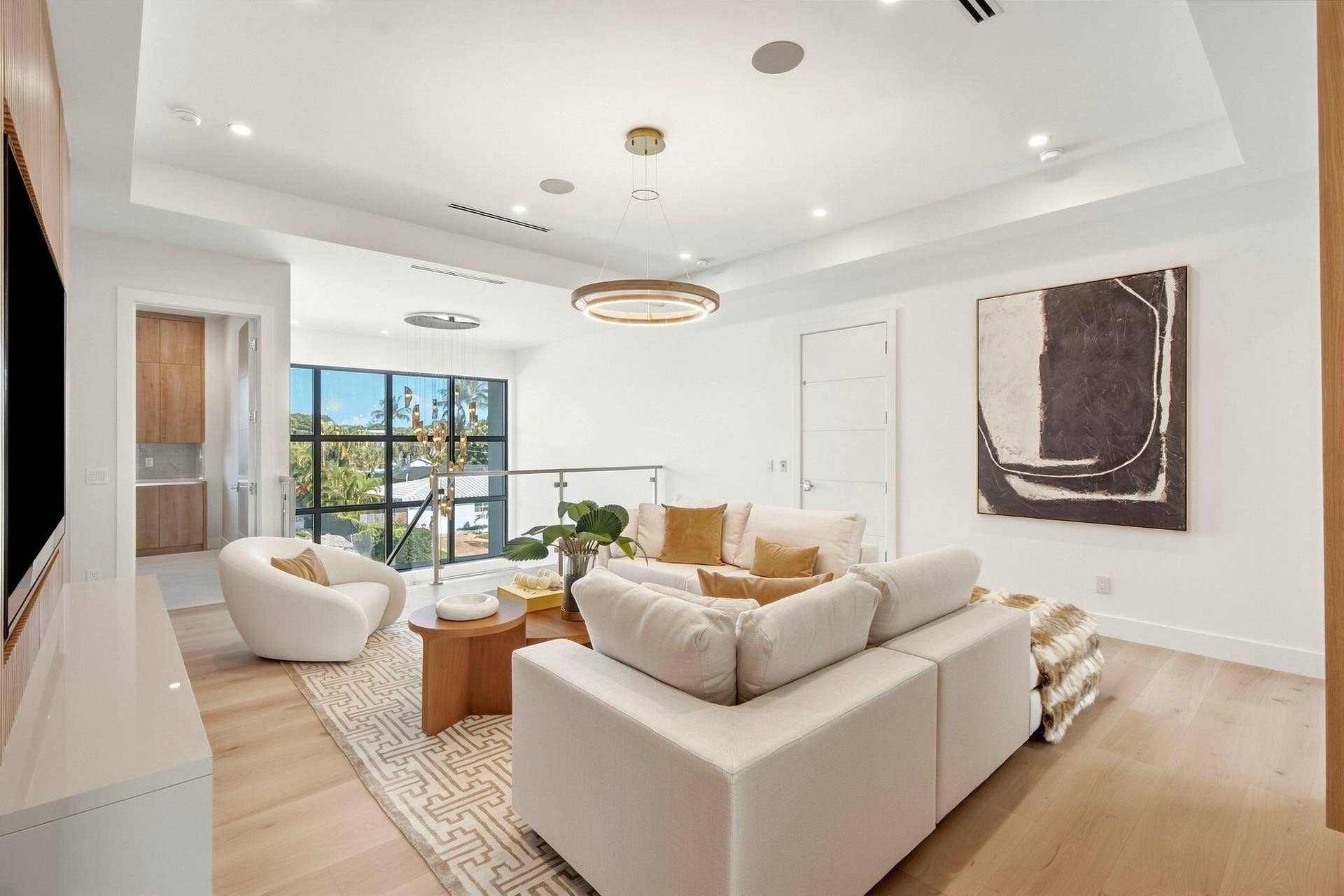 Spacious living area featuring light wood-finish flooring, a contemporary chandelier, recessed lighting, and a glass-paneled railing