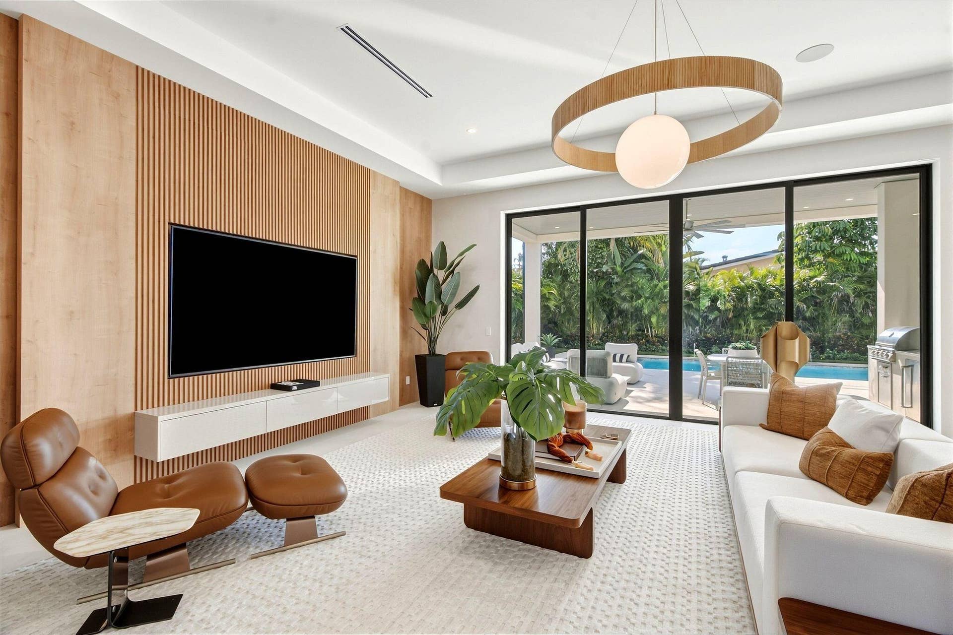 Wood slat accent wall, built-in entertainment console, recessed ceiling lighting, a contemporary chandelier, and sliding glass doors opening to outdoor living