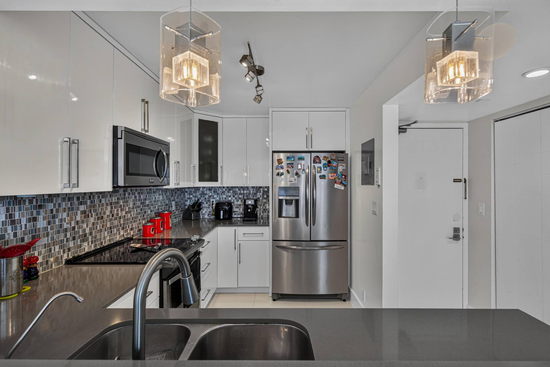 20379 W COUNTRY CLUB Drive, #1139, Aventura, FL 33180 Contemporary kitchen featuring high-gloss white cabinetry, mosaic tile backsplash, stainless steel appliances, and sleek pendant lighting