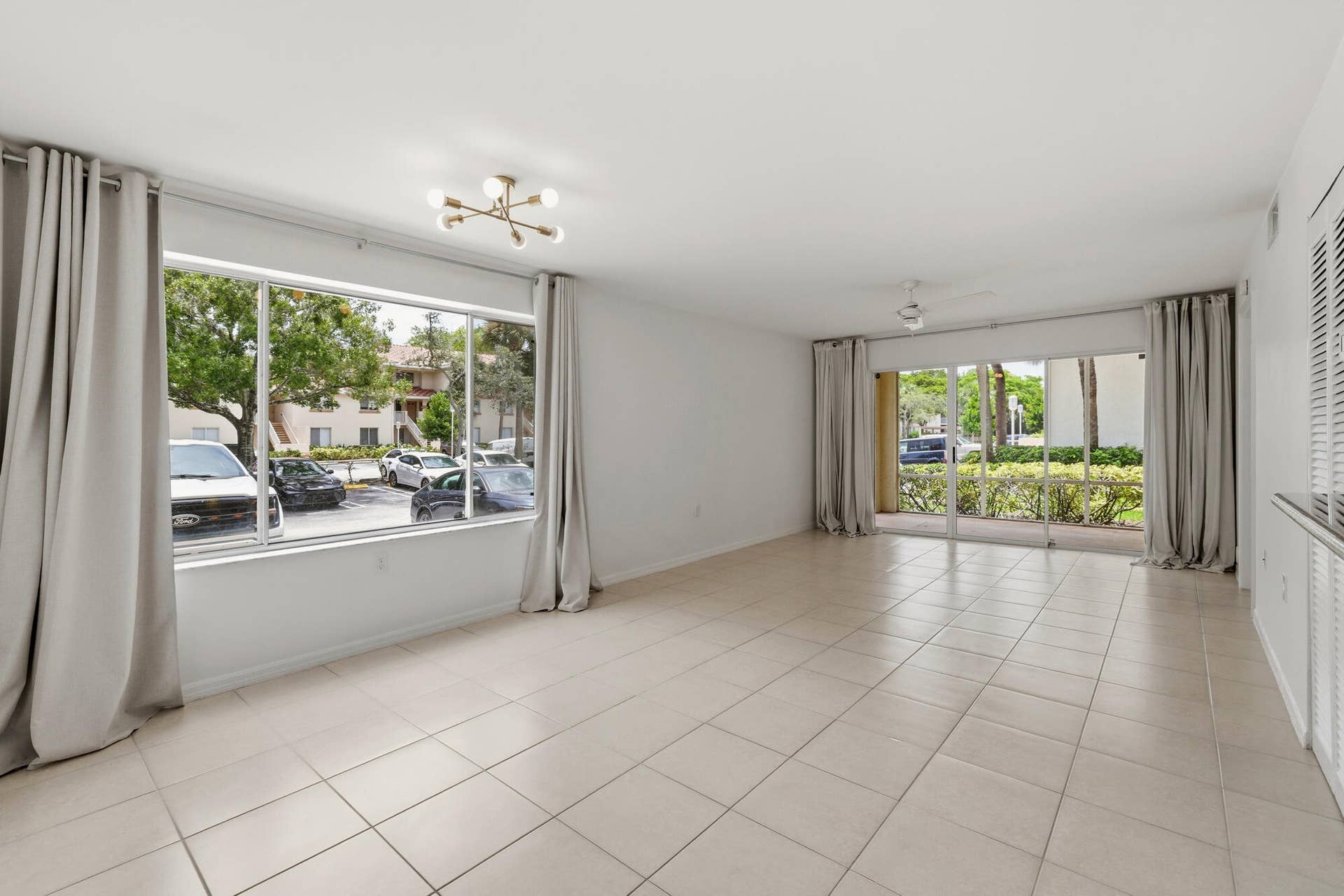 20101 Glenmoor Drive, West Palm Beach, West Palm Beach, FL 33409 Spacious living area featuring neutral tile flooring, a wide window with light-filtering drapes, and a contemporary ceiling fixture