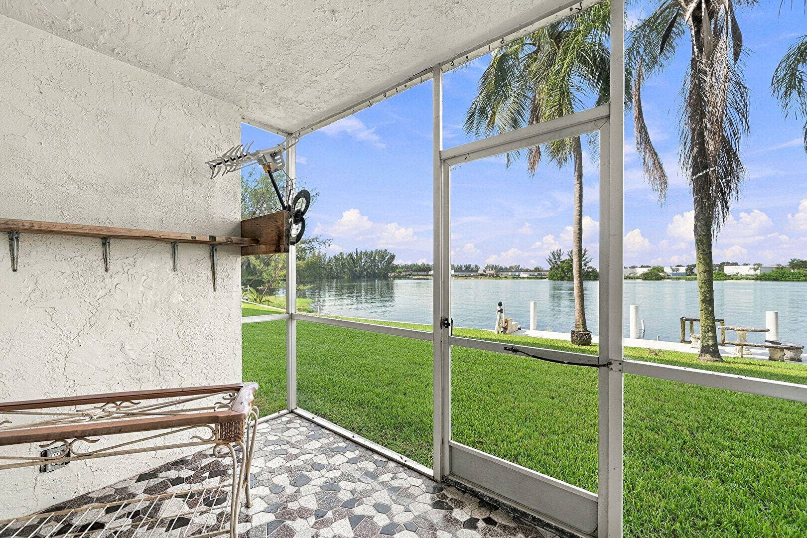 4311 CRYSTAL LAKE Drive, #110, Deerfield Beach, FL 33064 Screened patio with patterned tile flooring, offering direct access to a manicured lawn and waterfront
