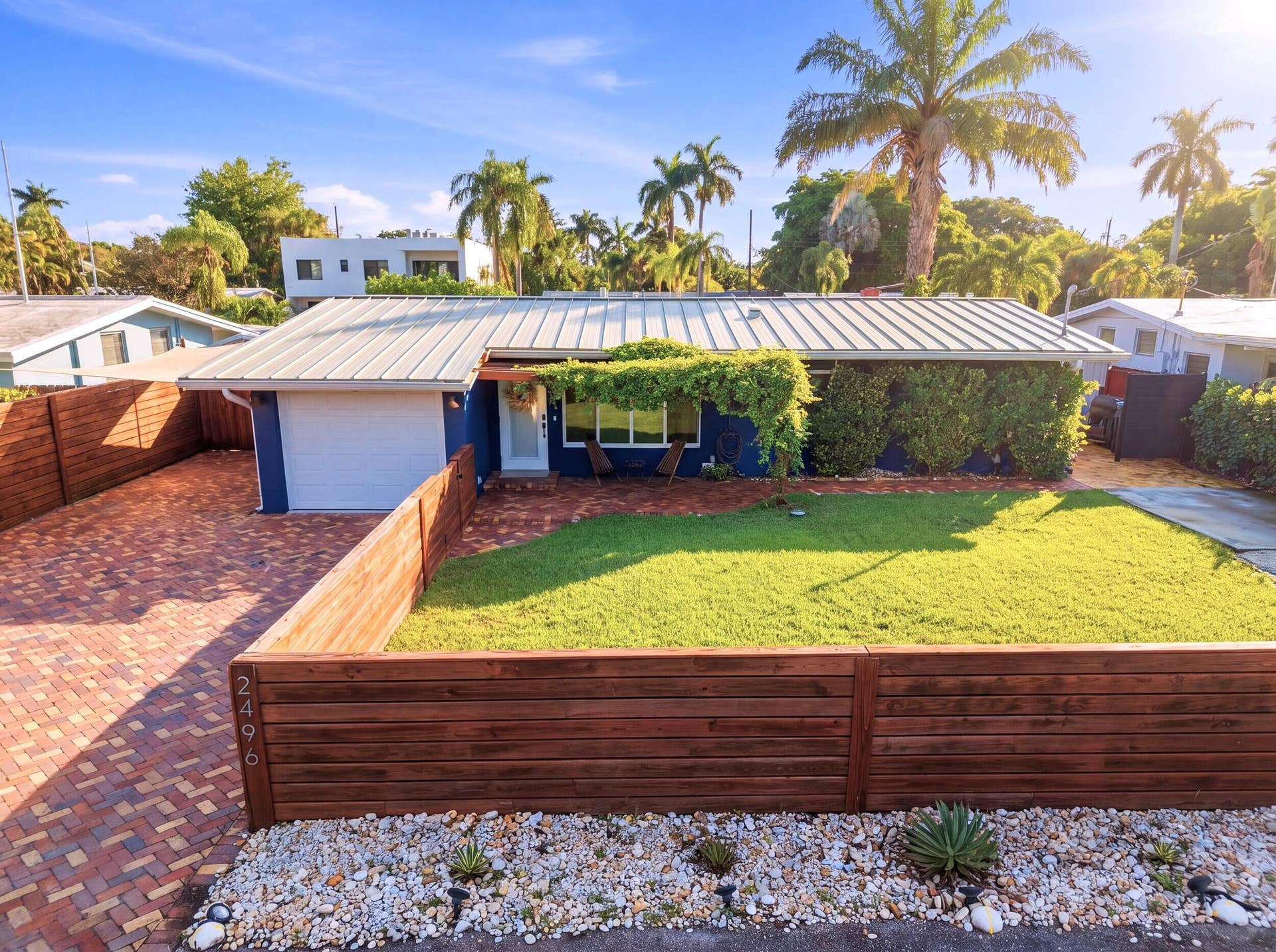 2496 BIMINI Lane, Fort Lauderdale, FL 33312 Metal roof, wood privacy fencing, brick paver driveway, manicured lawn, and lush landscaping