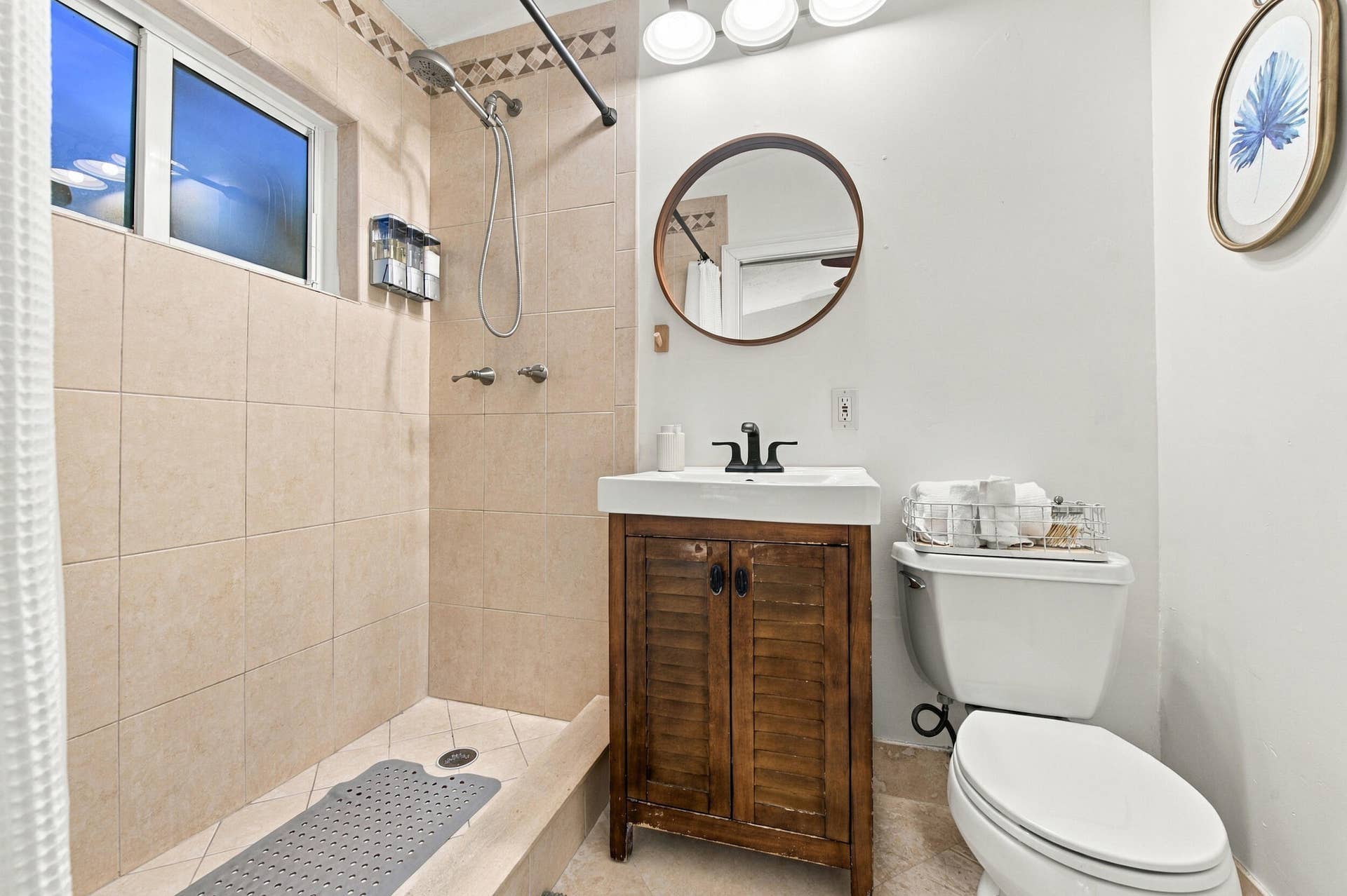 2496 BIMINI Lane, Fort Lauderdale, FL 33312 Walk-in shower with tiled walls, natural light window, dark wood-finish vanity with countertop sink, and a circular wall-mounted mirror