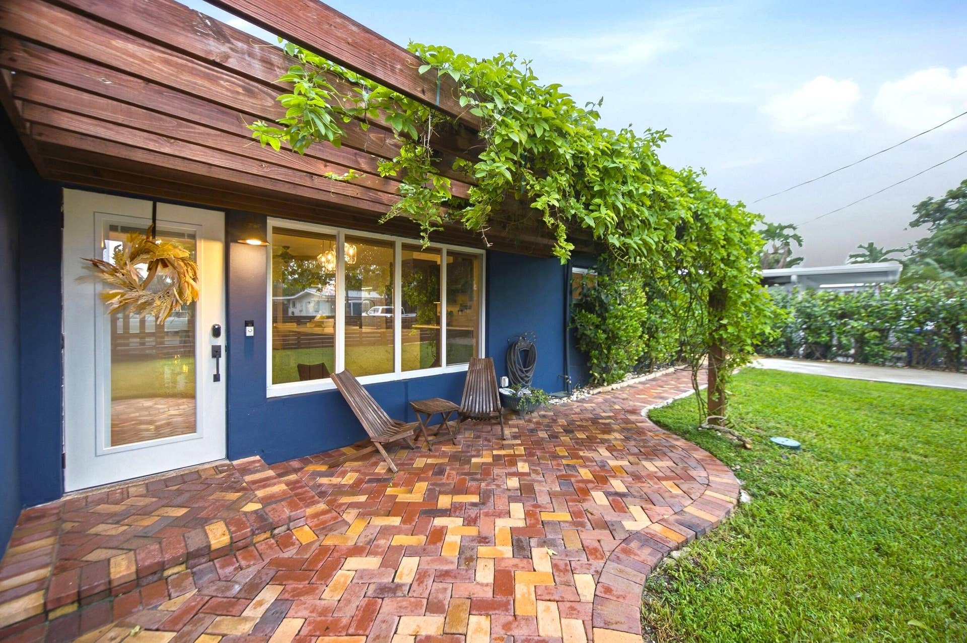 2496 BIMINI Lane, Fort Lauderdale, FL 33312 Wood pergola with lush greenery over a brick paver patio, featuring a full-light entry door and multiple windows