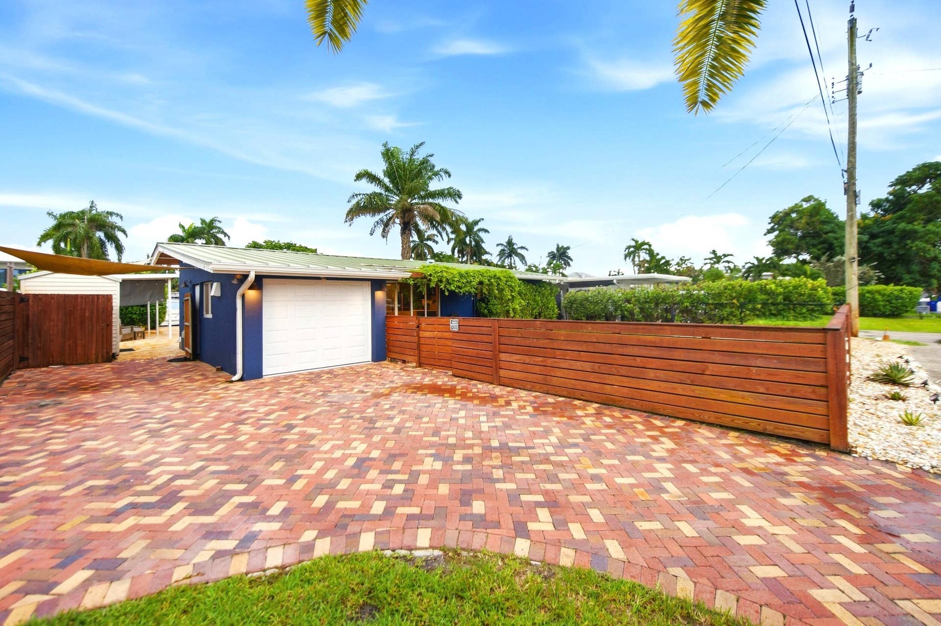 2496 BIMINI Lane, Fort Lauderdale, FL 33312 Herringbone brick paver driveway with a wood-slat fence and mature landscaping