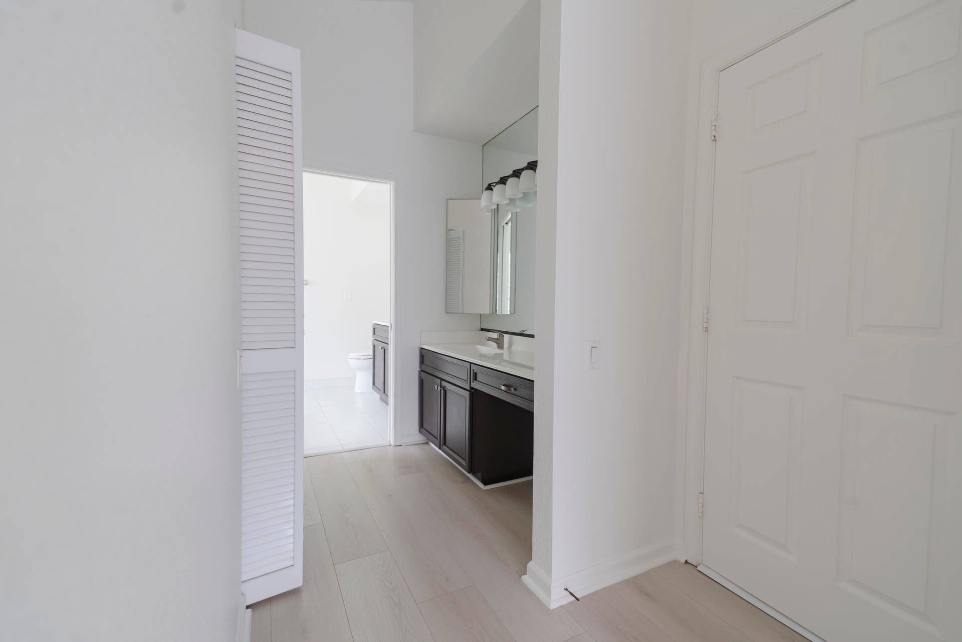 6162 BAY ISLES Drive, Boynton Beach, FL 33437 Wood-finish flooring, white paneled door, louvered bi-fold door, dark wood-finish vanity with countertop, and wall-mounted light fixture