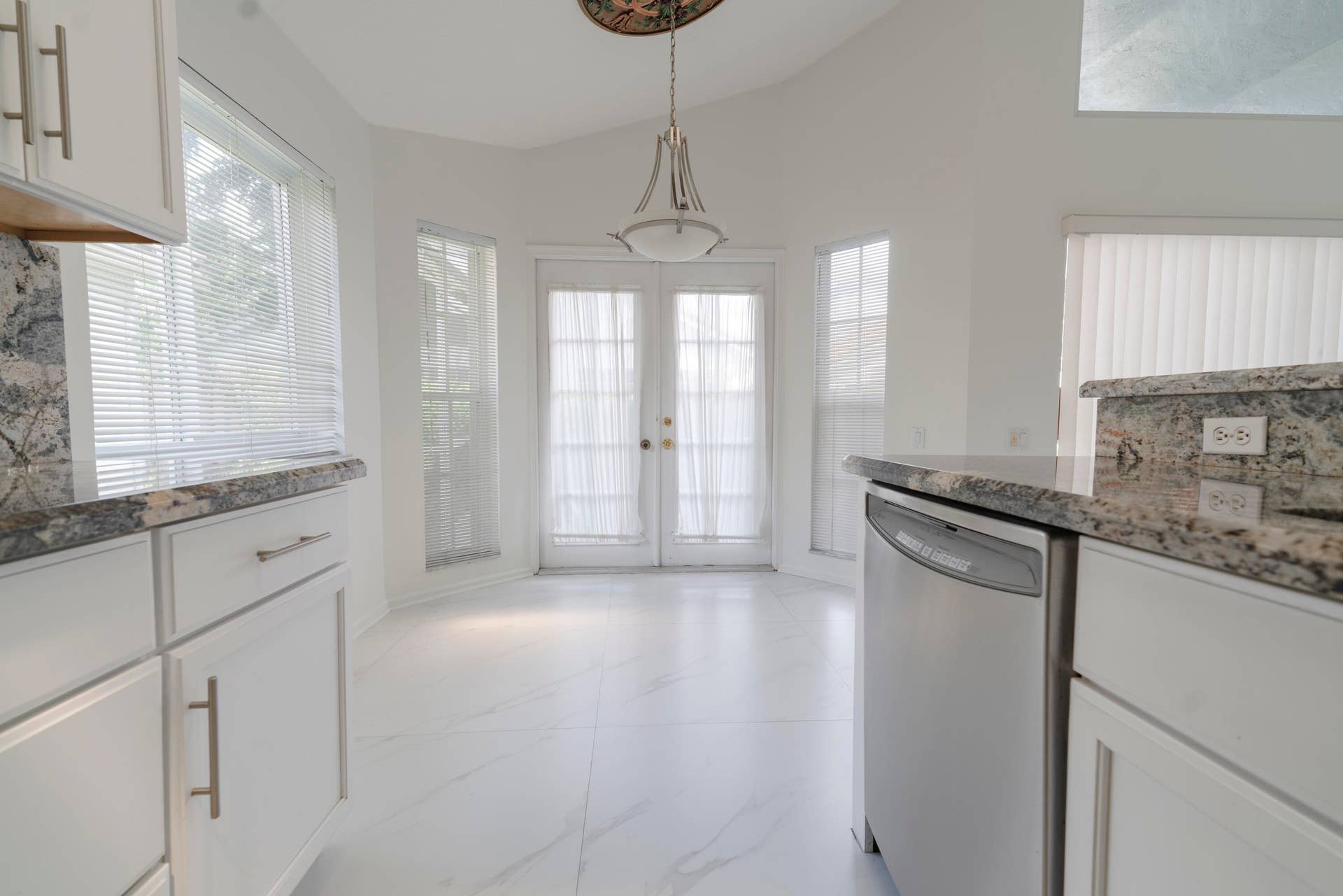 6162 BAY ISLES Drive, Boynton Beach, FL 33437 White cabinetry with brushed nickel hardware, granite countertops, stainless steel dishwasher, white tile flooring, and double French doors