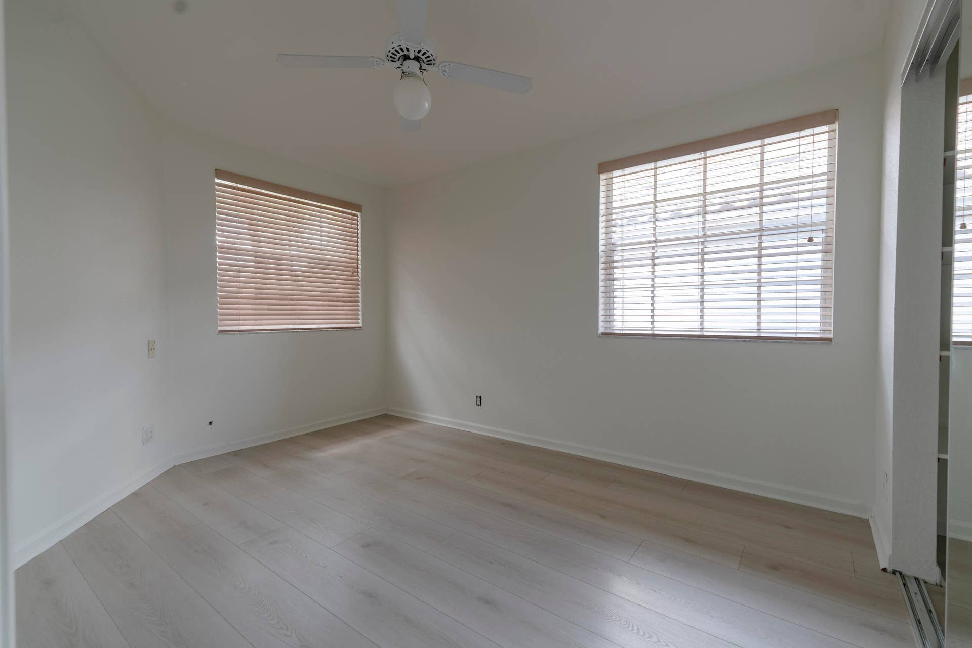 6162 BAY ISLES Drive, Boynton Beach, FL 33437 Light wood-finish flooring, white walls, two windows with blinds, ceiling fan with integrated lighting, and mirrored closet doors