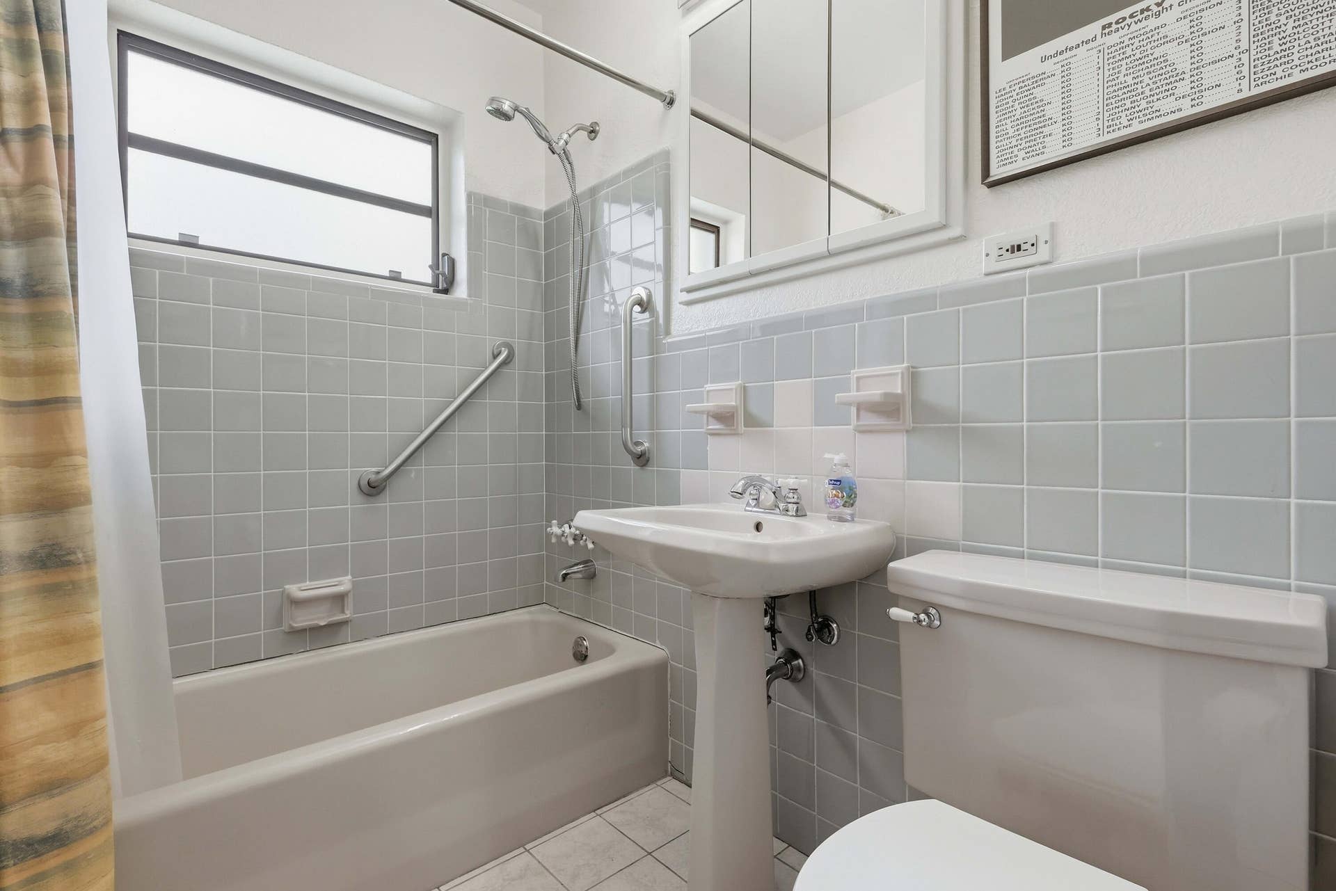 Bathroom featuring a pedestal sink, white ceramic toilet, bathtub with shower fixture, and a window