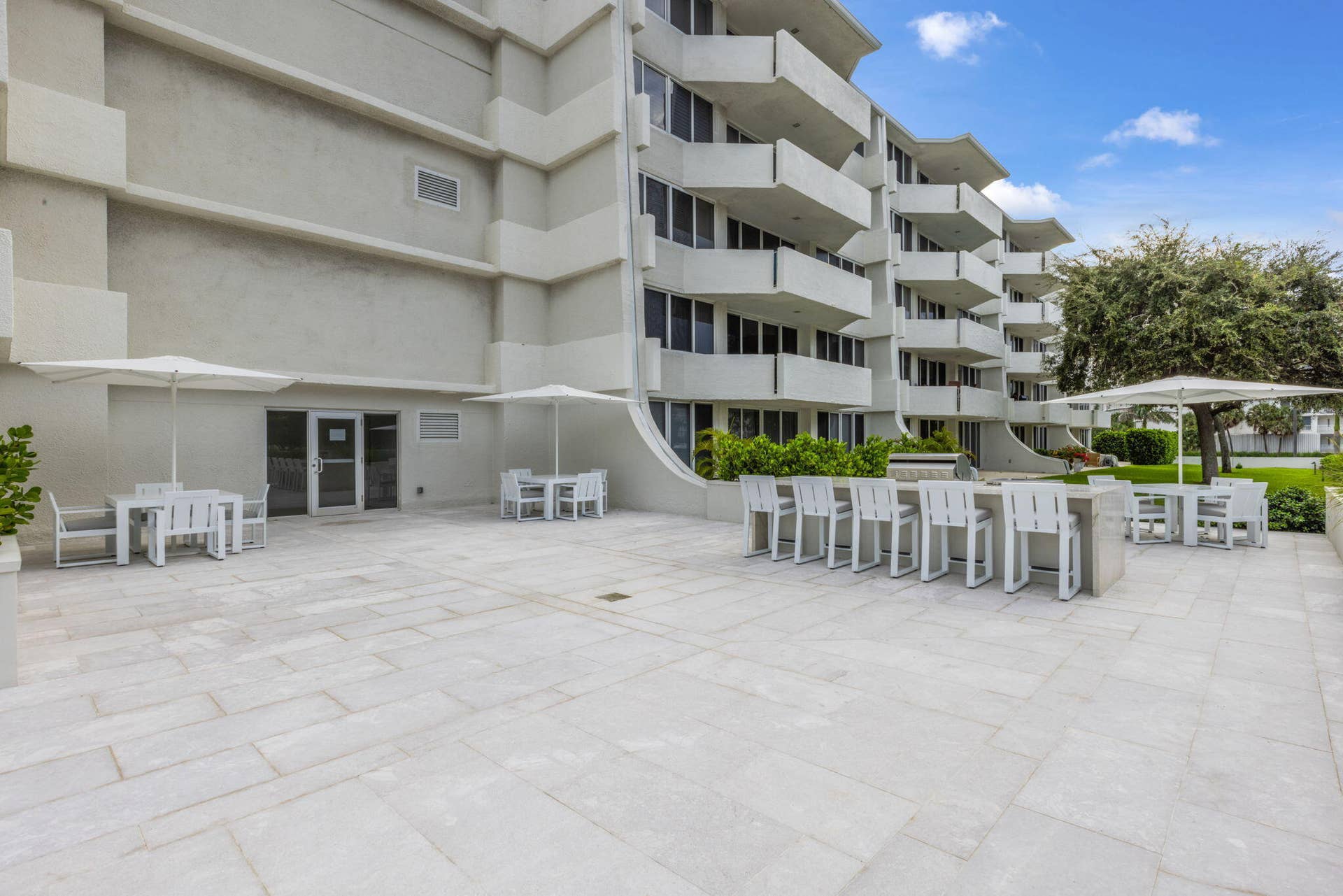 2773 S Ocean Boulevard, #517, Palm Beach, Palm Beach, FL 33480 Expansive outdoor patio with stone-finish pavers, multiple seating areas, a built-in bar, and a multi-story building exterior with individual balconies