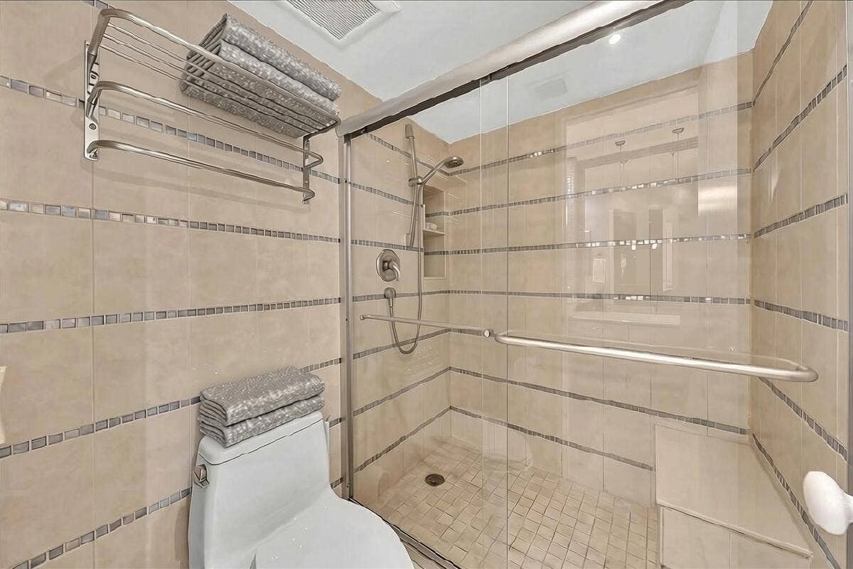 3505 Oaks Way, #109, Pompano Beach, FL 33069 Glass-enclosed shower with a built-in bench and tiled walls with decorative mosaic accents