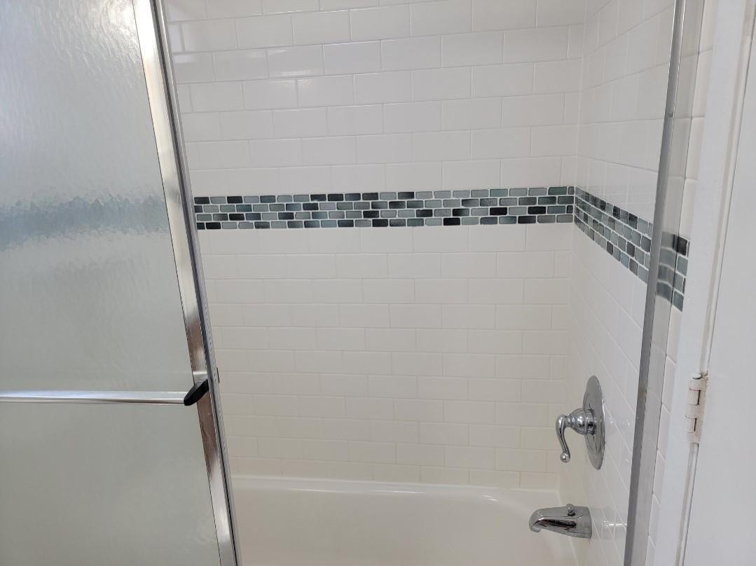 1001 SE 6TH Avenue, #127, Deerfield Beach, Deerfield Beach, FL 33441 Bathtub with white subway tile surround, decorative mosaic tile accent band, polished chrome fixtures, and frosted glass shower enclosure