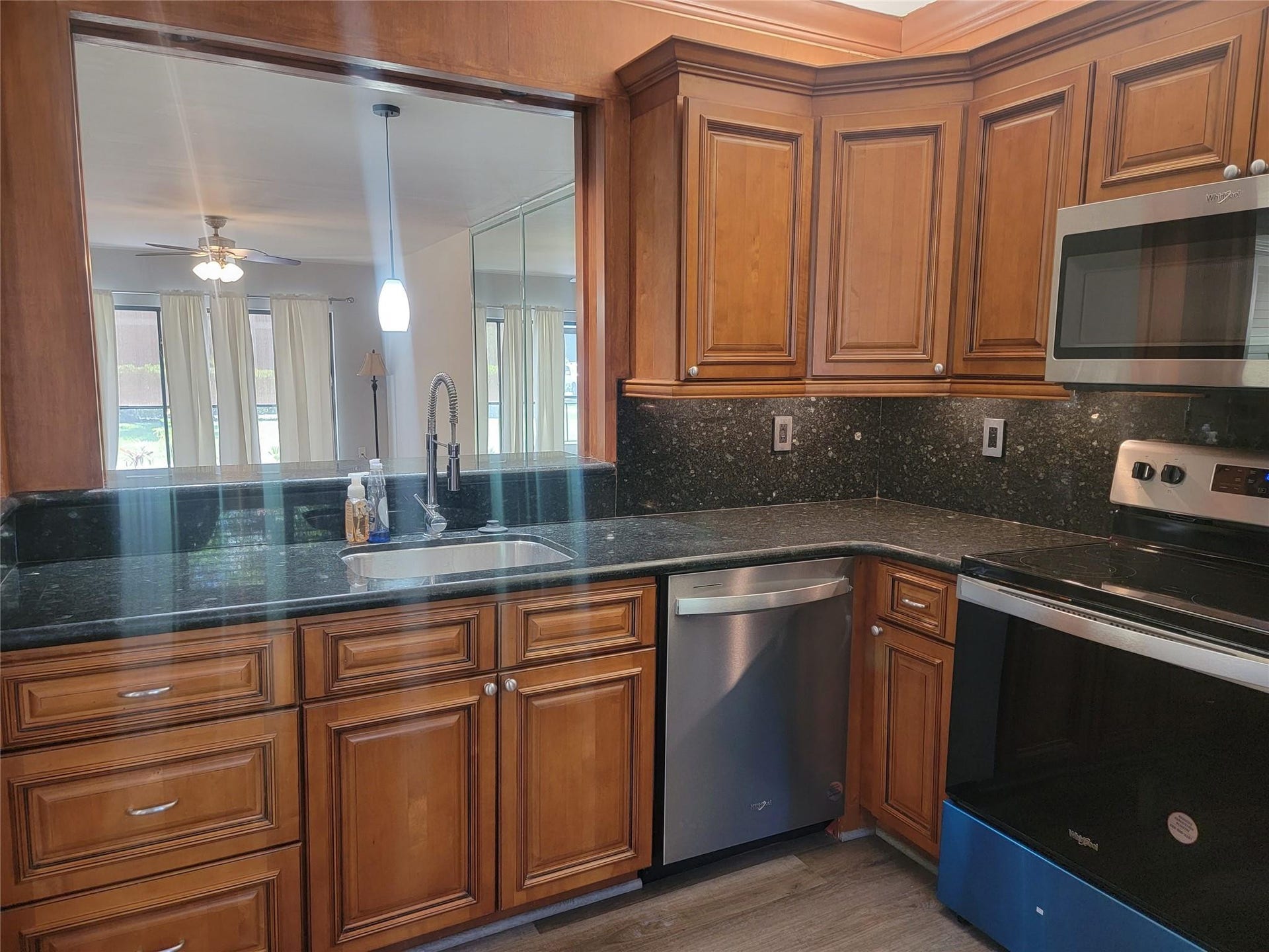1001 SE 6TH Avenue, #127, Deerfield Beach, Deerfield Beach, FL 33441 Wood-finish cabinetry with stainless steel hardware, dark countertops with matching backsplash, stainless steel appliances, and a pass-through window with a pendant light fixture