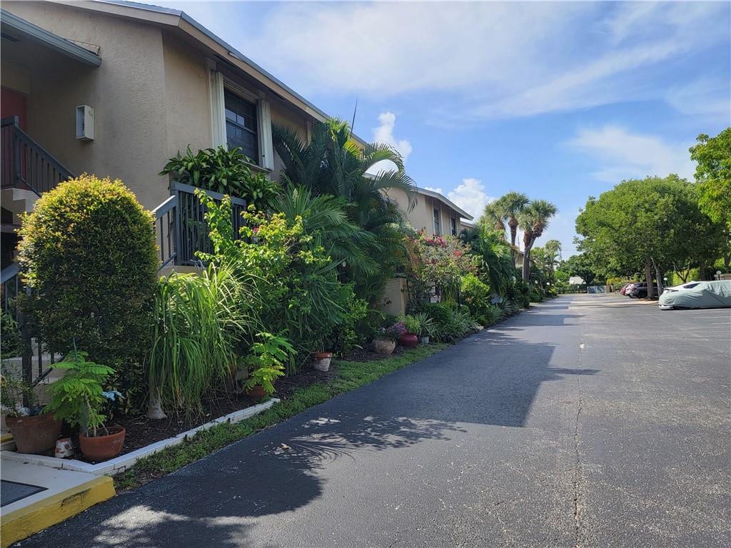 1001 SE 6TH Avenue, #127, Deerfield Beach, Deerfield Beach, FL 33441 Stucco exterior building with a pitched roofline, surrounded by dense tropical landscaping, paved driveway, and mature trees