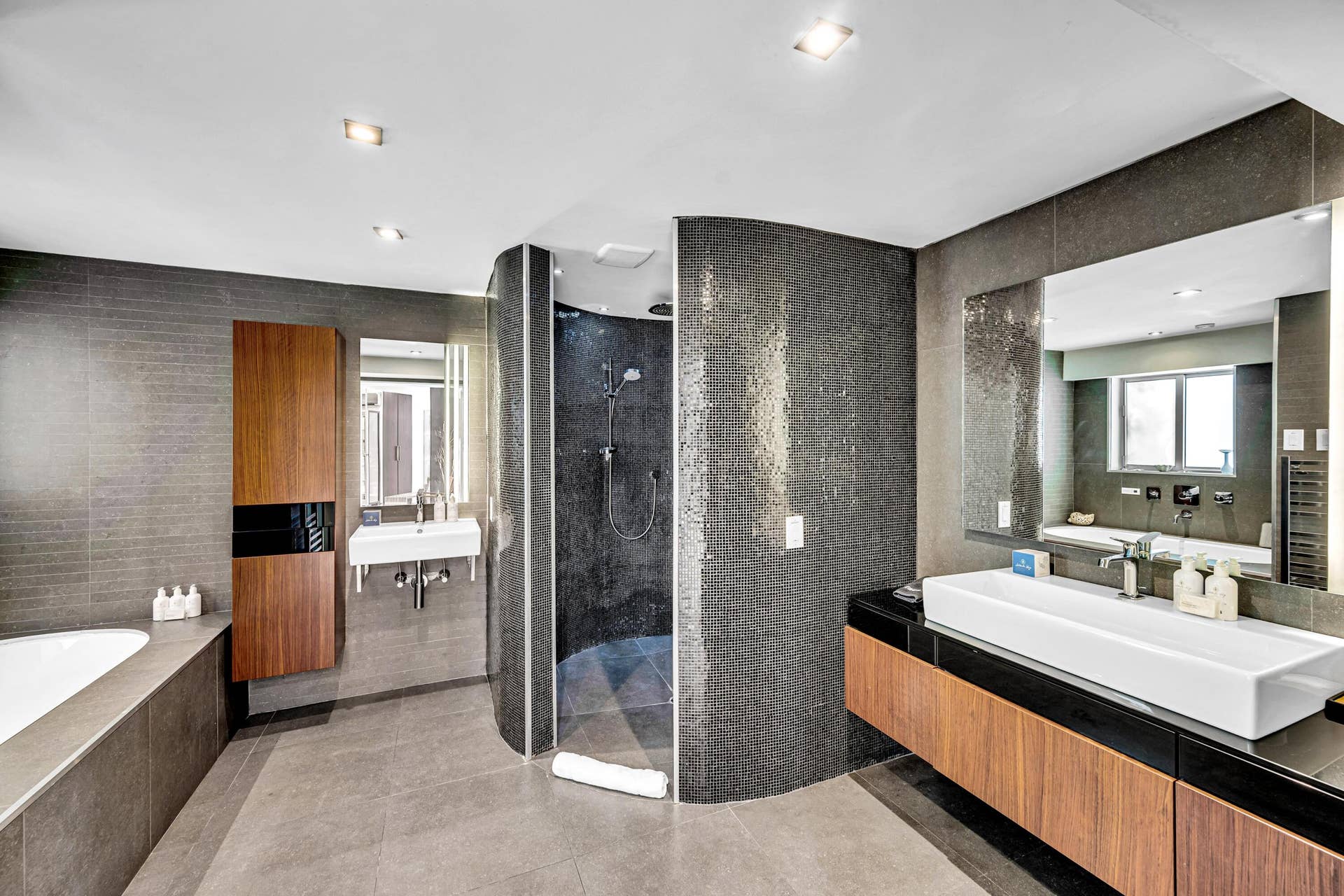 510 SW 18th Avenue, Fort Lauderdale, FL 33312 Curved tile shower enclosure with dark mosaic tile, dual wall-mounted sinks, wood-finish vanity with a vessel sink, recessed lighting, and a built-in soaking tub