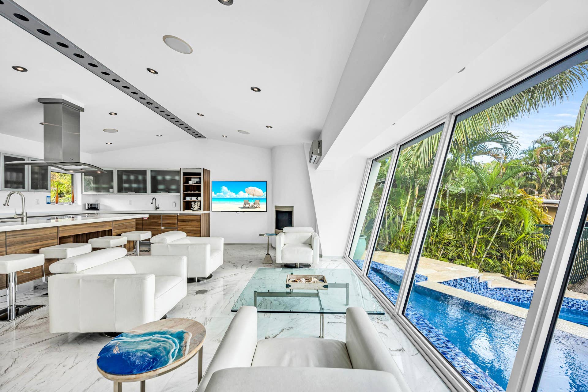 510 SW 18th Avenue, Fort Lauderdale, FL 33312 Open-concept living space with large format tile flooring, a contemporary kitchen featuring a stainless steel range hood, and extensive floor-to-ceiling windows overlooking a built-in swimming pool