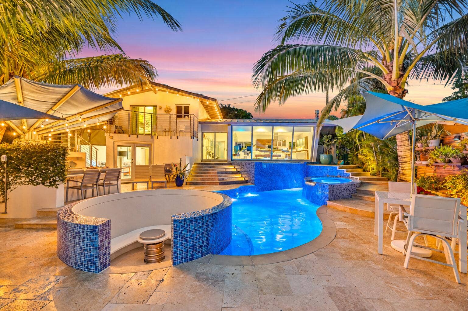 510 SW 18th Avenue, Fort Lauderdale, FL 33312 Curved swimming pool with blue tile accents, adjacent spa, integrated seating area, and multiple water features, surrounded by stone-finish paving