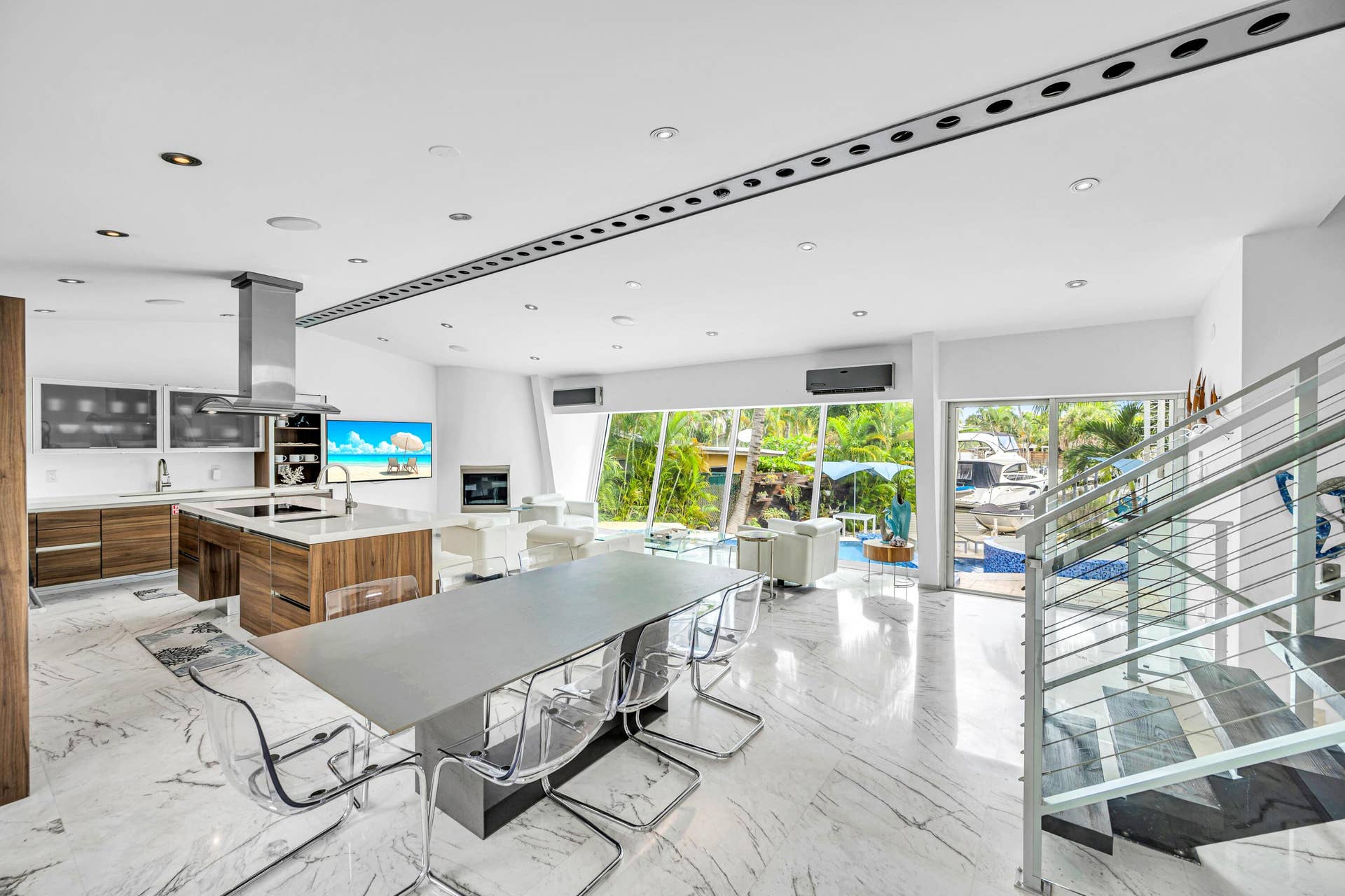 510 SW 18th Avenue, Fort Lauderdale, FL 33312 Open-concept living area with polished marble flooring, a modern kitchen island with wood-finish cabinetry, a stainless steel range hood, and a contemporary glass and metal staircase