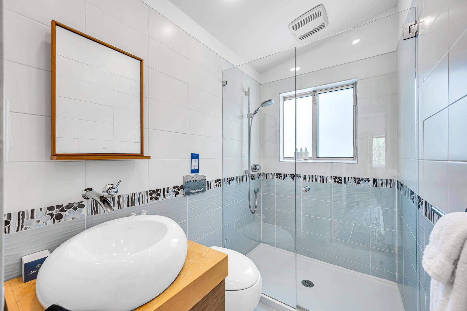 510 SW 18th Avenue, Fort Lauderdale, FL 33312 Glass-enclosed shower with a rainfall showerhead and a window, complemented by a vessel sink atop a wood-finish vanity, and a wall-mounted mirror with a wood frame