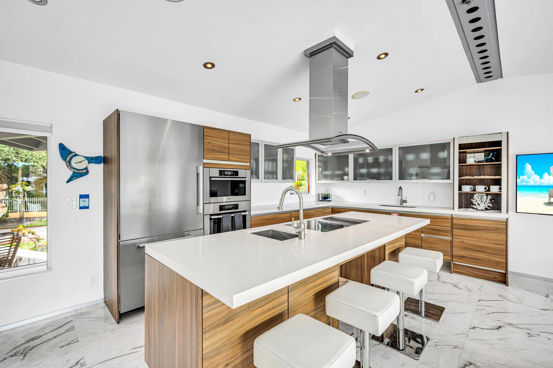 510 SW 18th Avenue, Fort Lauderdale, FL 33312 Sleek kitchen with a central island featuring dual sinks, a stainless steel range hood, built-in stainless steel appliances, wood-finish cabinetry, and white countertops