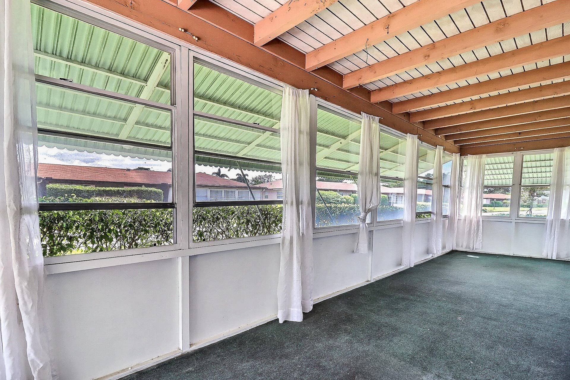 450 BLUEBIRD Lane, Delray Beach, FL 33445 Screened enclosure with an exposed wood beam ceiling, multiple awning windows, and a green carpeted floor