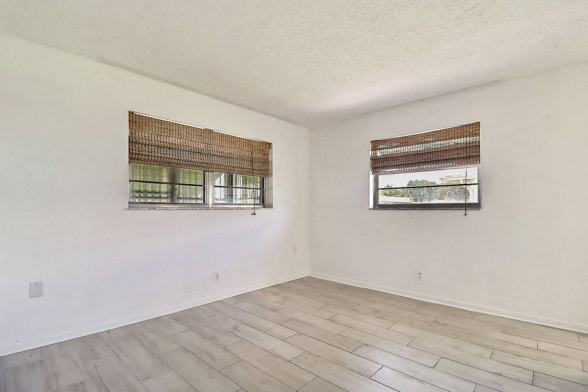 450 BLUEBIRD Lane, Delray Beach, FL 33445 White walls with two large windows featuring woven blinds, wood-finish plank flooring, and a textured ceiling