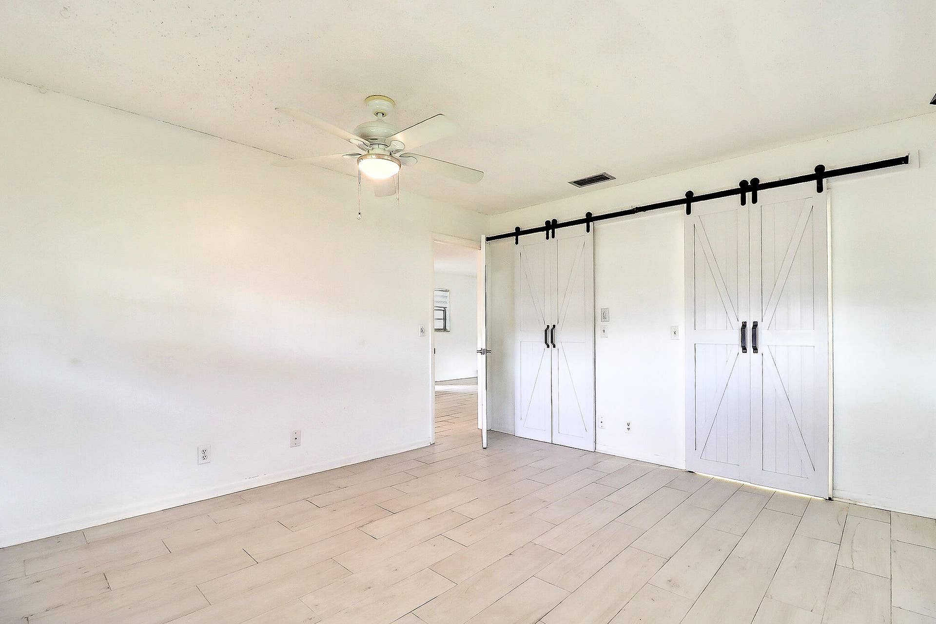 450 BLUEBIRD Lane, Delray Beach, FL 33445 White wood-finish flooring, two sets of white barn doors with black hardware, and a ceiling fan with integrated lighting