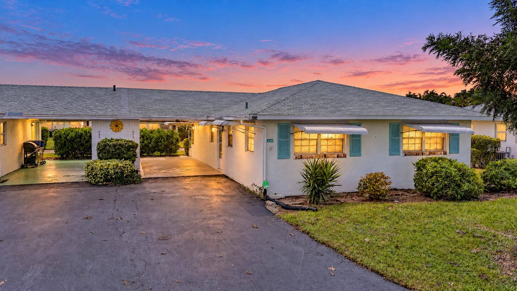 450 BLUEBIRD Lane, Delray Beach, FL 33445 White exterior with light blue window shutters and awnings, asphalt driveway, covered carport, and established landscaping