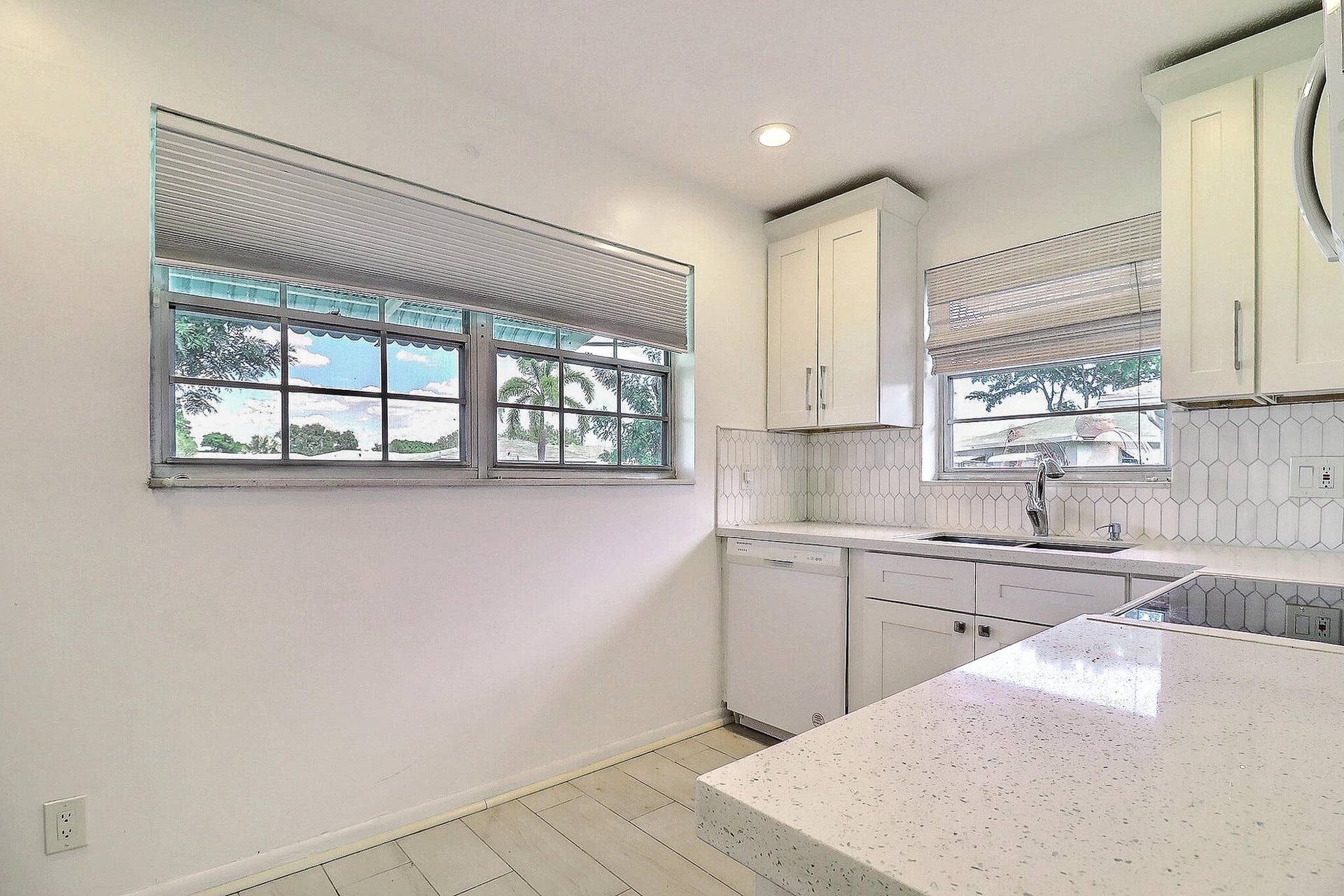 450 BLUEBIRD Lane, Delray Beach, FL 33445 White shaker cabinetry, light-toned countertops, white subway tile backsplash, stainless steel sink with a gooseneck faucet, and integrated dishwasher