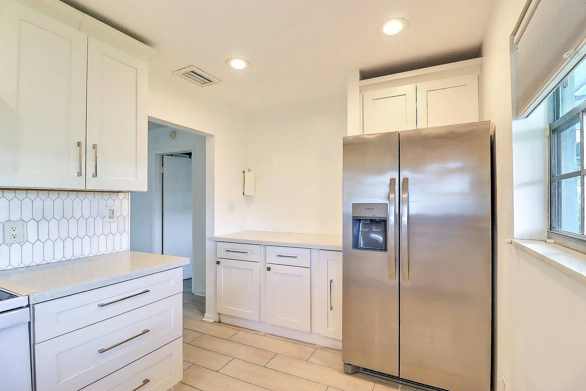 450 BLUEBIRD Lane, Delray Beach, FL 33445 White shaker cabinetry, light-toned countertops, geometric tile backsplash, recessed lighting, and stainless steel refrigerator