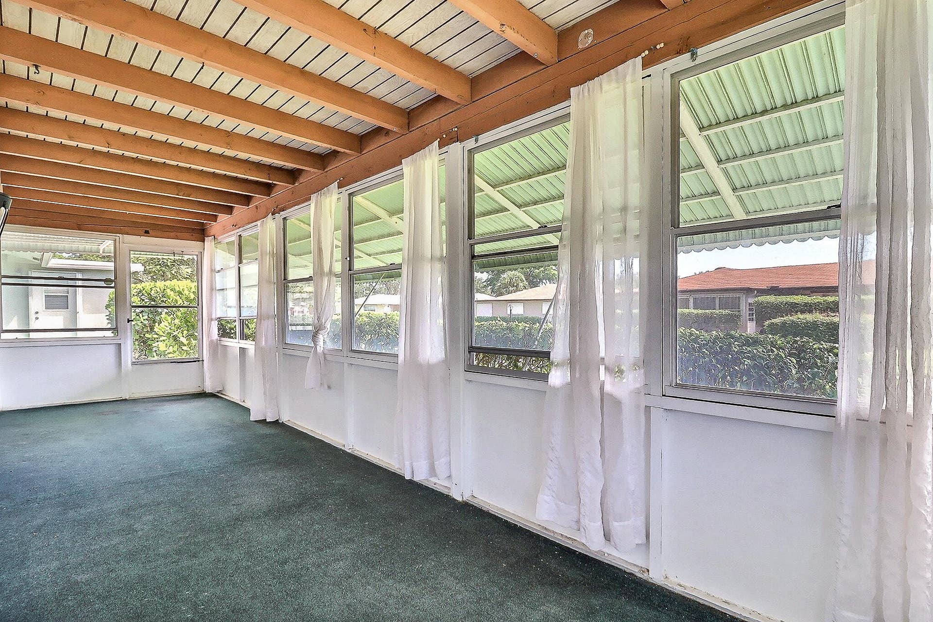 450 BLUEBIRD Lane, Delray Beach, FL 33445 Enclosed porch with exposed wood beam ceiling, white paneled walls, multiple windows, and green carpeting