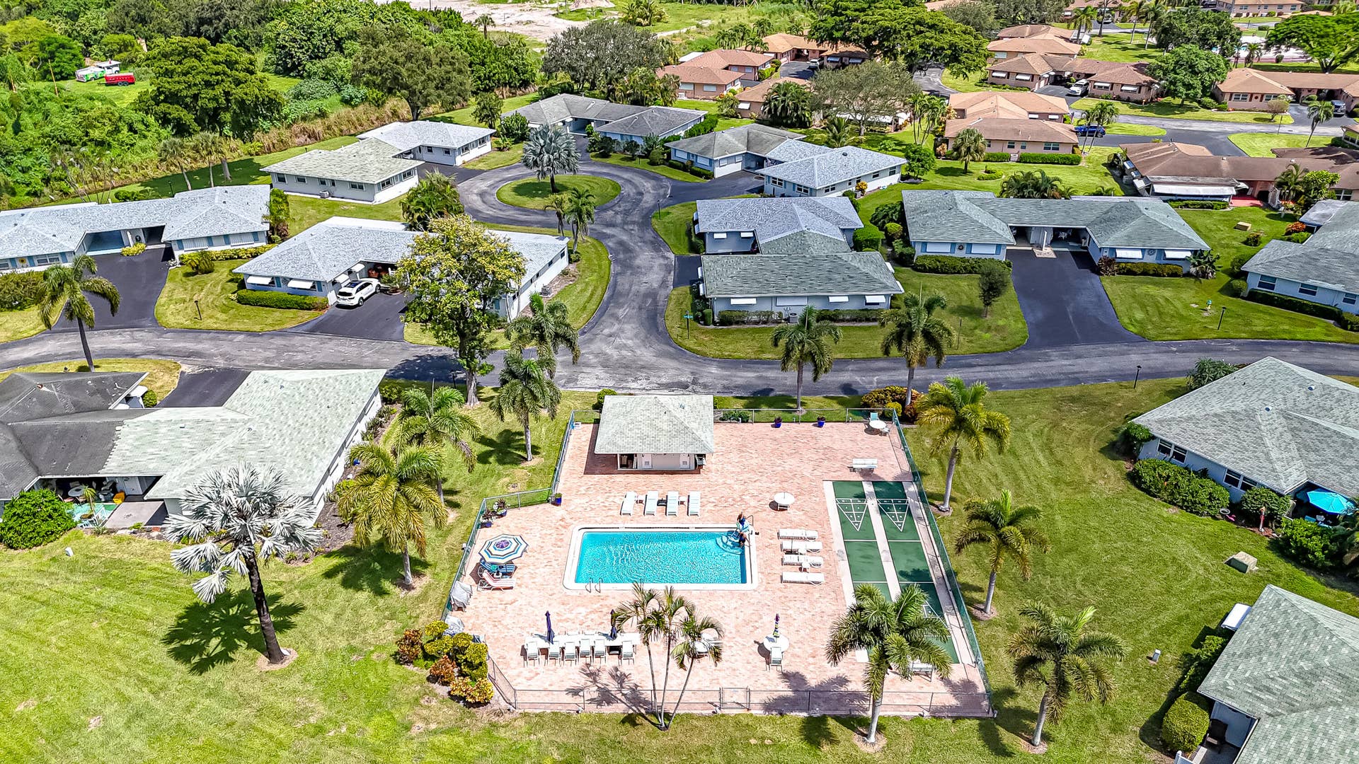 450 BLUEBIRD Lane, Delray Beach, FL 33445 Community setting featuring a central swimming pool, paved pool deck, shuffleboard courts, mature palm trees, and single-story residences