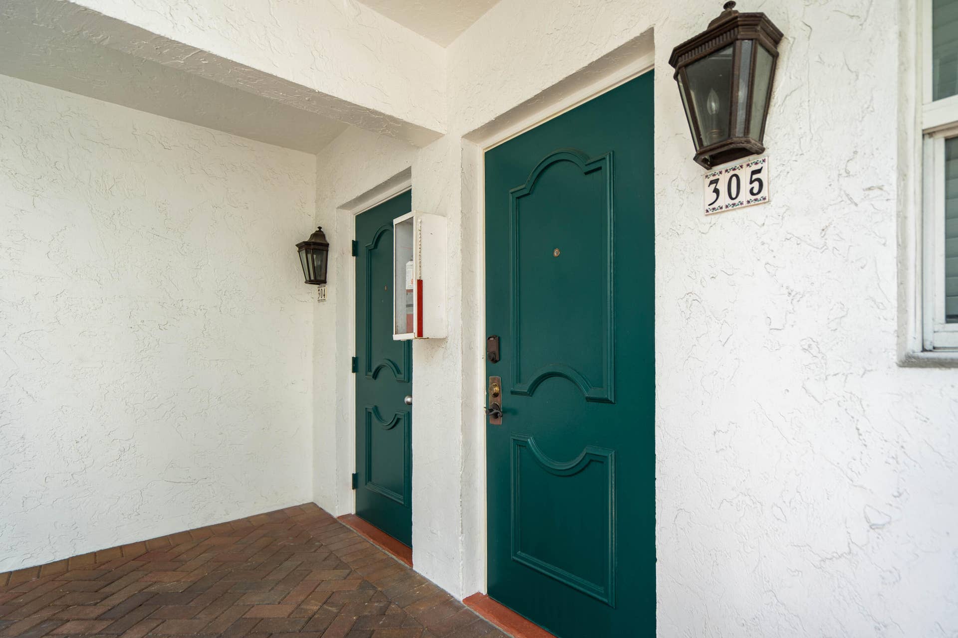 Welcoming entry foyer featuring dual teal-painted panel doors with decorative molding, warm wood-finish flooring, white textured walls, and vintage-style wall-mounted lantern sconces