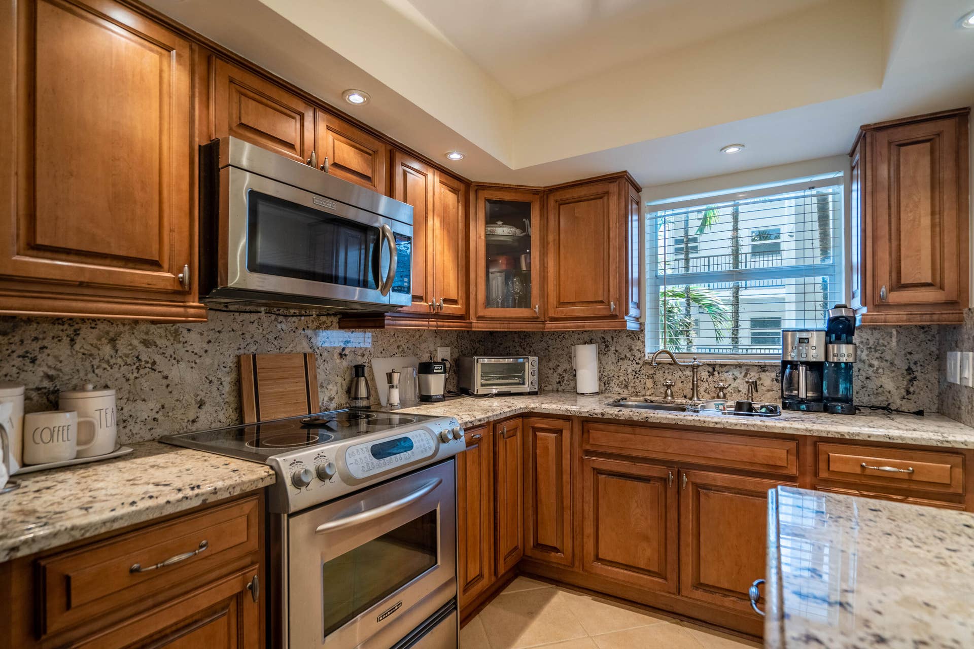 Hardwood cabinetry with stainless steel appliances, granite countertops, and a full-height granite backsplash