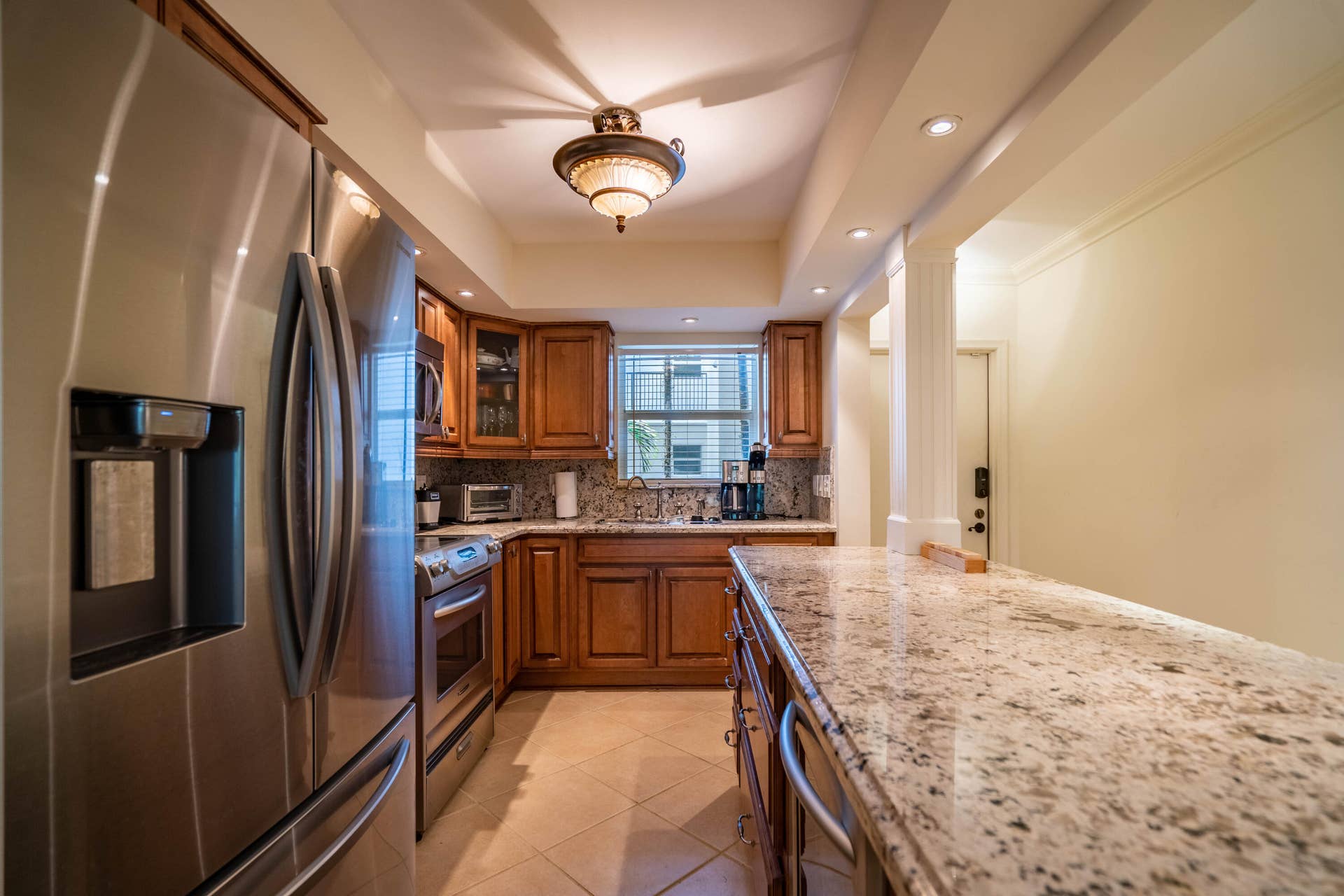 Stainless steel refrigerator, granite countertops, tile flooring, wood cabinetry, and recessed lighting