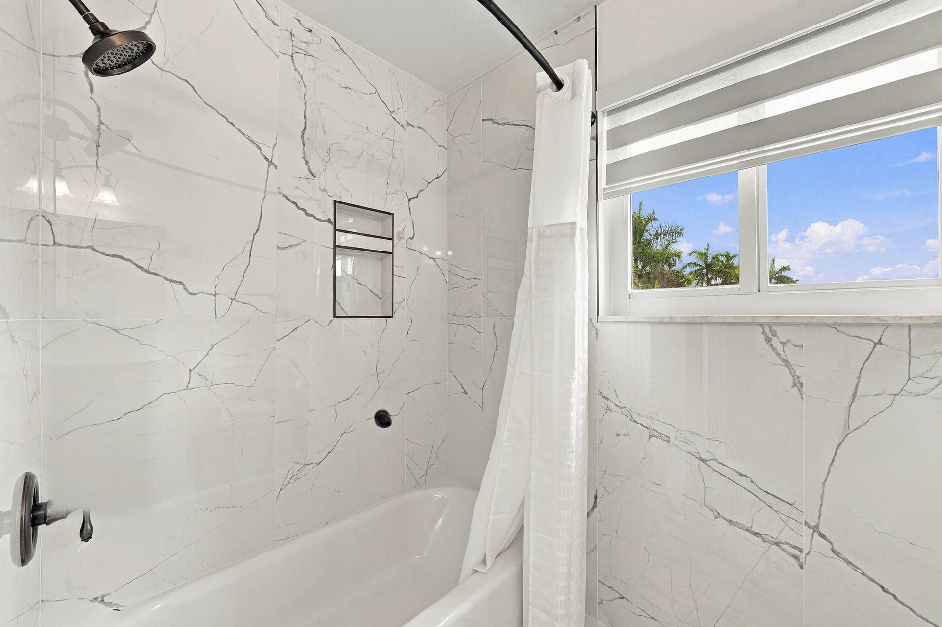 1020 Lavender Circle, Weston, FL 33327 Bathtub and shower combination featuring floor-to-ceiling veined wall tile, built-in shower niche, and a window with a roller shade