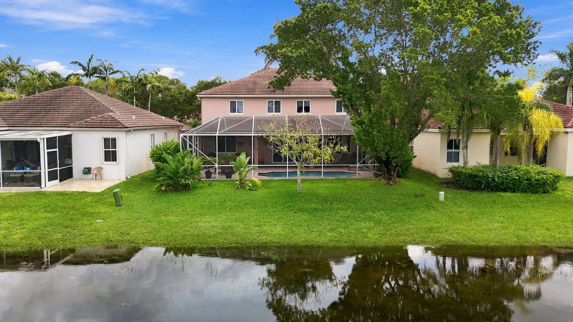 1020 Lavender Circle, Weston, FL 33327 Waterfront property featuring a screened-in pool, expansive green lawn, mature trees, and a screened patio