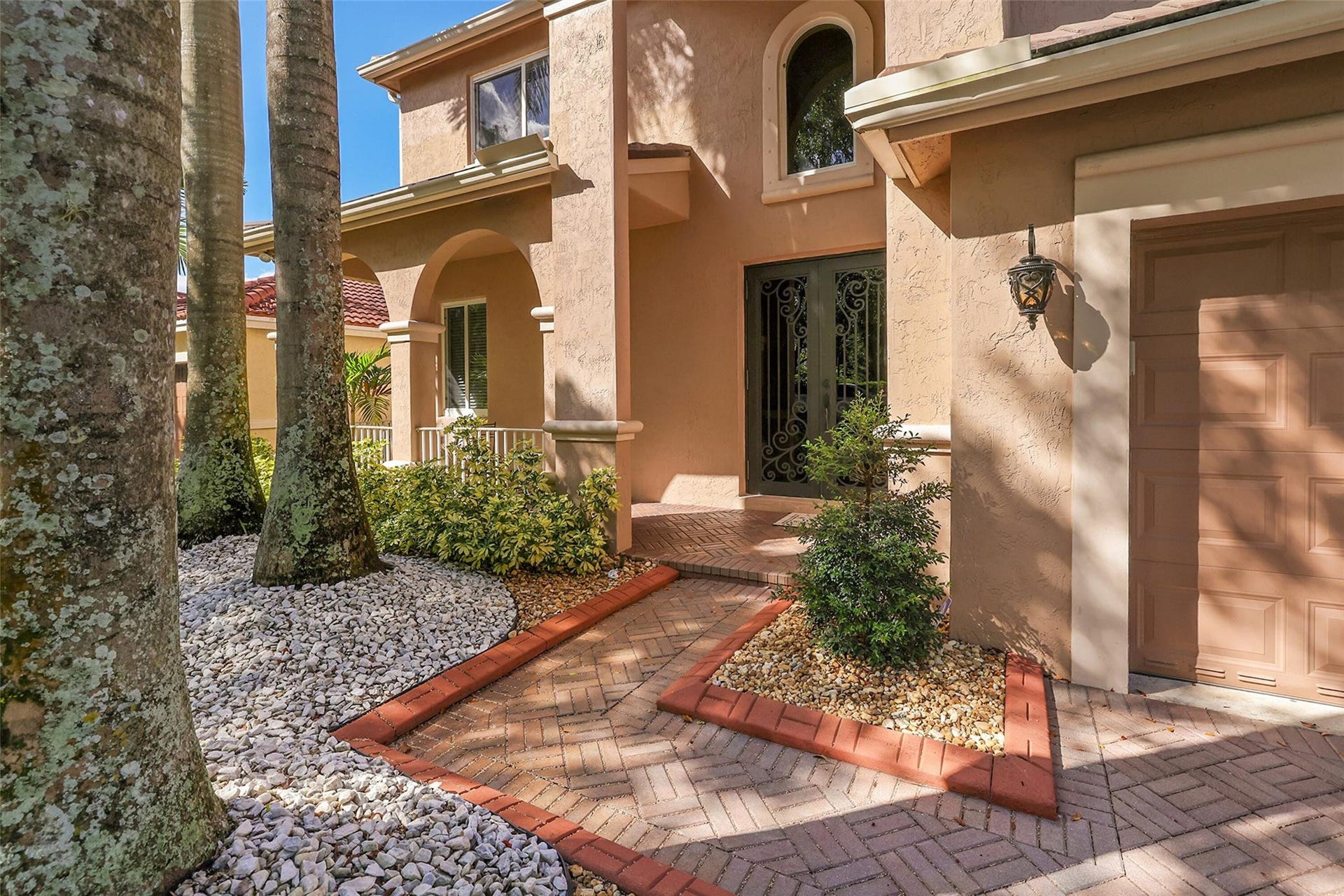 1020 Lavender Circle, Weston, FL 33327 Stucco exterior with arched entryway, decorative wrought iron double doors, brick paver walkway, and garage with exterior lighting
