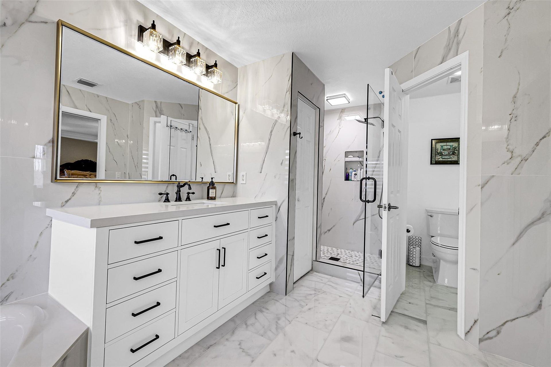 1020 Lavender Circle, Weston, FL 33327 Spacious bathroom featuring a glass-enclosed shower, dual-sink vanity with ample storage, large framed mirror, and contemporary lighting fixtures