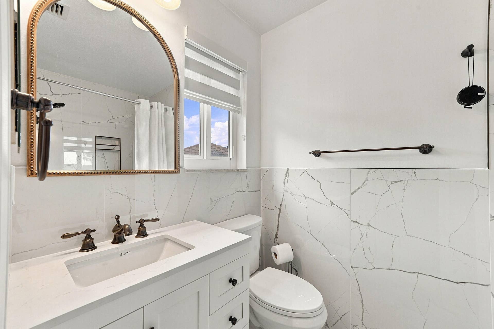 1020 Lavender Circle, Weston, FL 33327 White vanity with an integrated sink, bronze-finish faucet, arched mirror, and marble-look wall tile