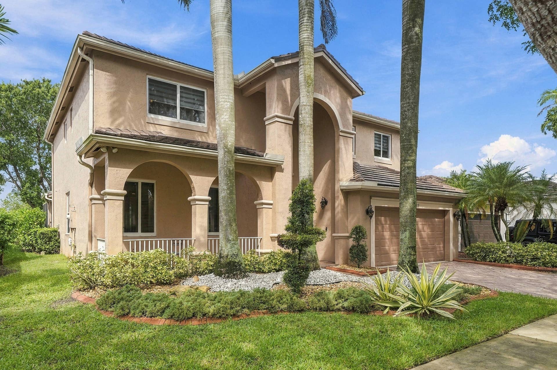 1020 Lavender Circle, Weston, FL 33327 Two-story stucco exterior featuring a two-car garage, arched entryways, tile roofing, and mature landscaping