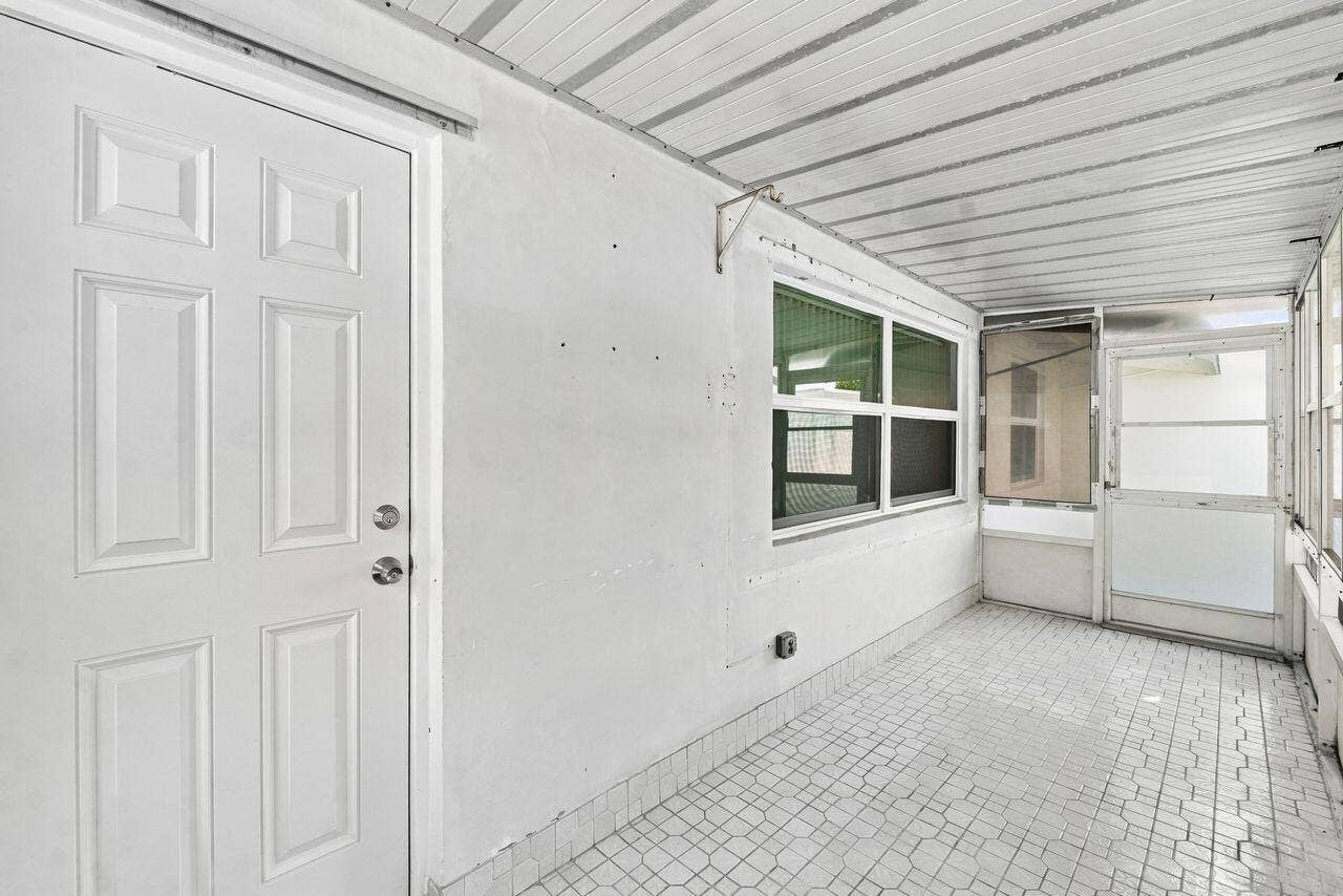 1003 SW 17th Street, Boynton Beach, FL 33426 Enclosed patio featuring a white paneled door, multiple windows, a screened door, and patterned tile flooring