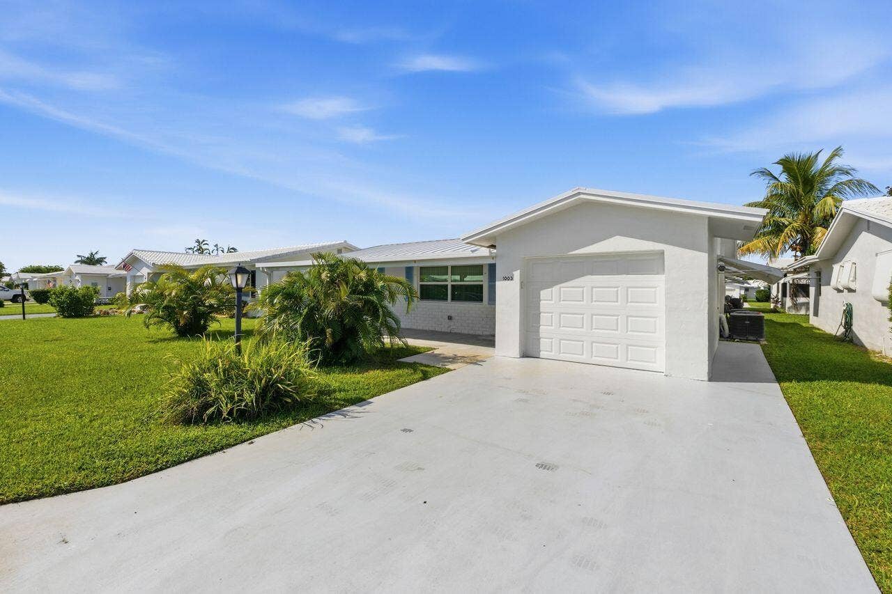 1003 SW 17th Street, Boynton Beach, FL 33426 White stucco exterior, attached garage, expanded concrete driveway, manicured lawn, and mature landscaping