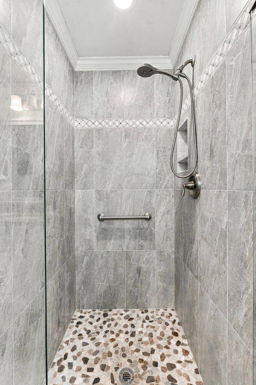 1003 SW 17th Street, Boynton Beach, FL 33426 Glass-enclosed shower featuring large format tile walls, decorative accent tile, a built-in shower niche, and a pebble-tiled floor
