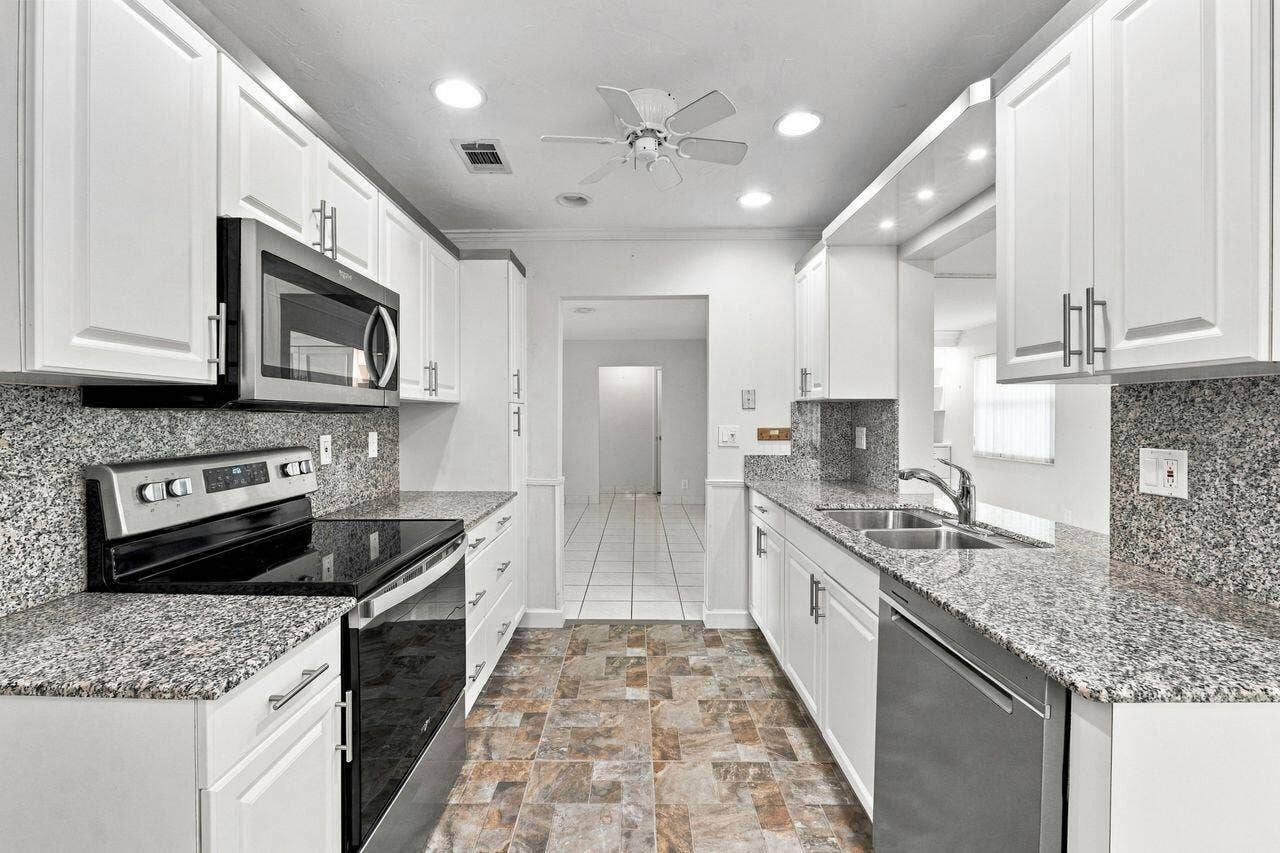 1003 SW 17th Street, Boynton Beach, FL 33426 Galley kitchen with white cabinetry, granite countertops, stainless steel appliances, and ceiling fan