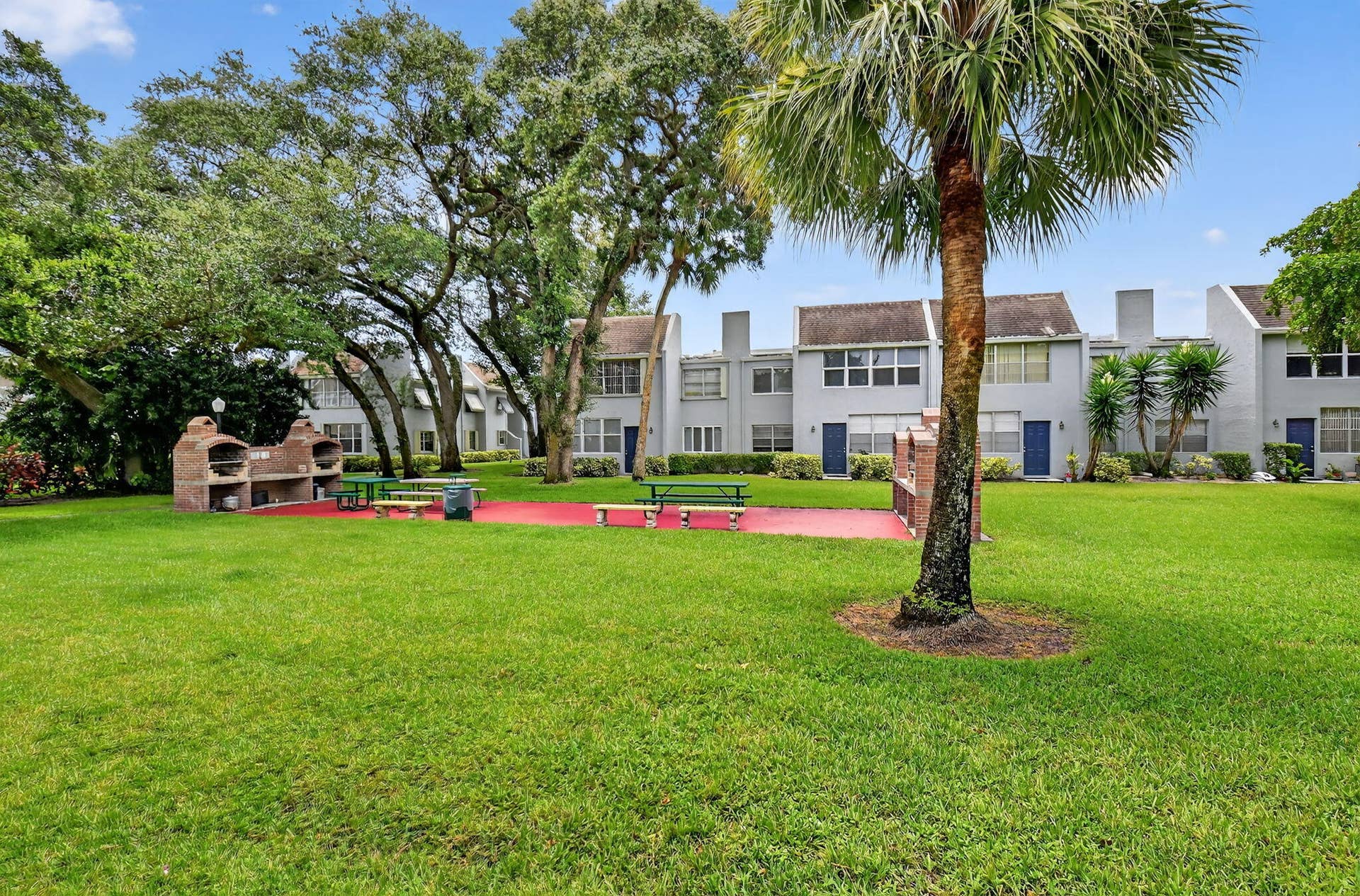 2320 SW 22nd Avenue, #211, Delray Beach, FL 33445 Expansive grassy area featuring mature trees, a built-in outdoor grill station, and picnic tables