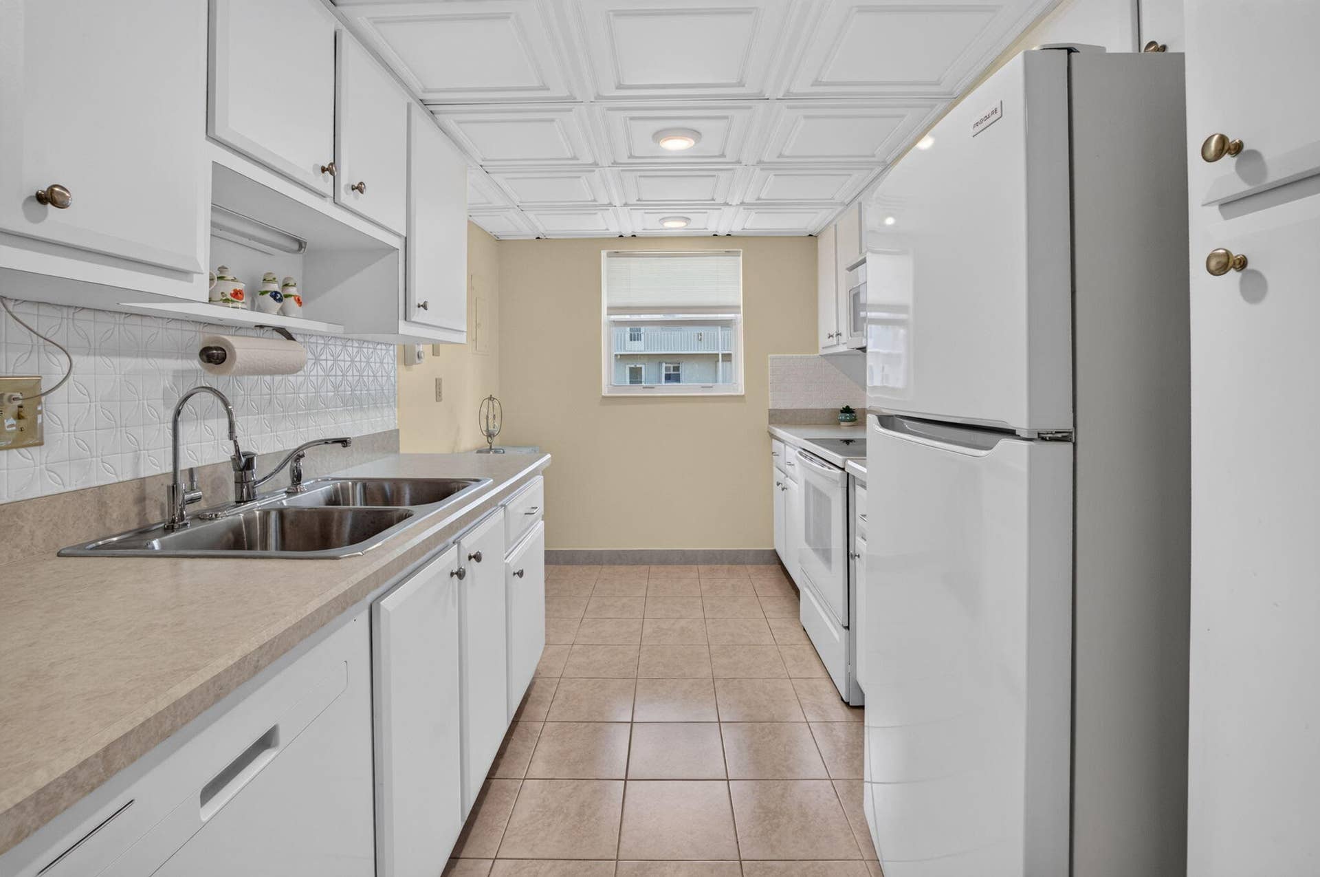 2320 SW 22nd Avenue, #211, Delray Beach, FL 33445 Galley kitchen featuring white cabinetry, a double basin sink, a large white refrigerator, and tiled flooring