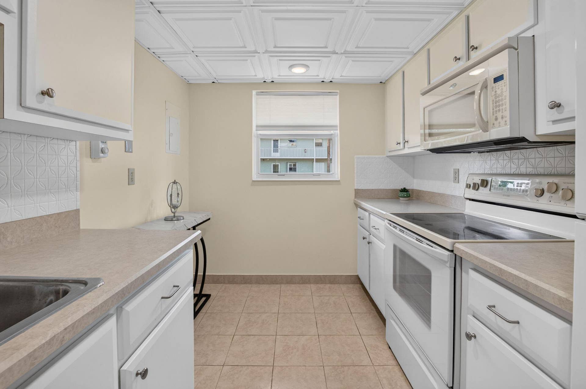2320 SW 22nd Avenue, #211, Delray Beach, FL 33445 Kitchen featuring white cabinetry, light-toned countertops, tile flooring, and a patterned backsplash